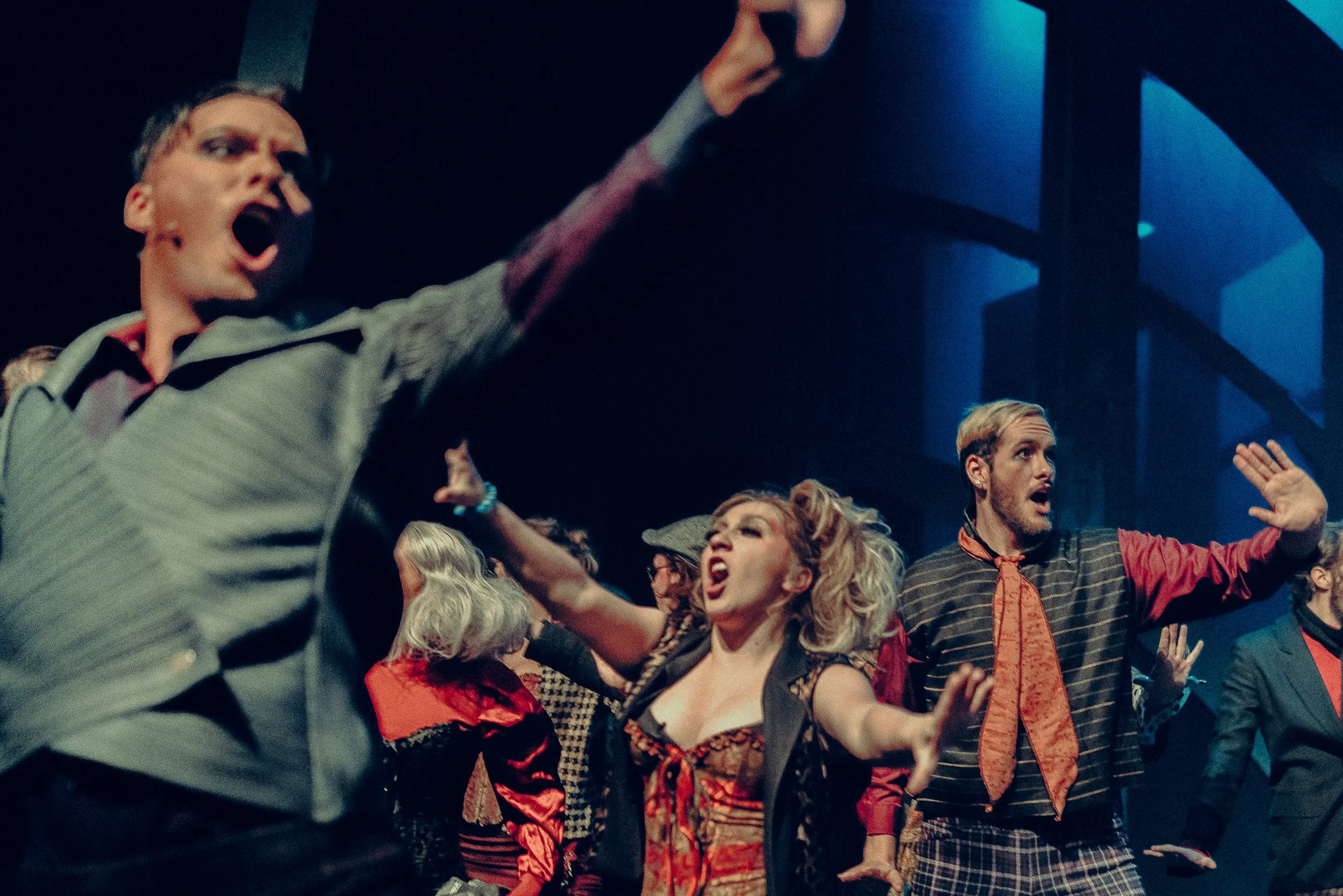 Theatrical performance with actors on stage wearing colorful costumes, singing or acting with expressive gestures, under dramatic lighting.