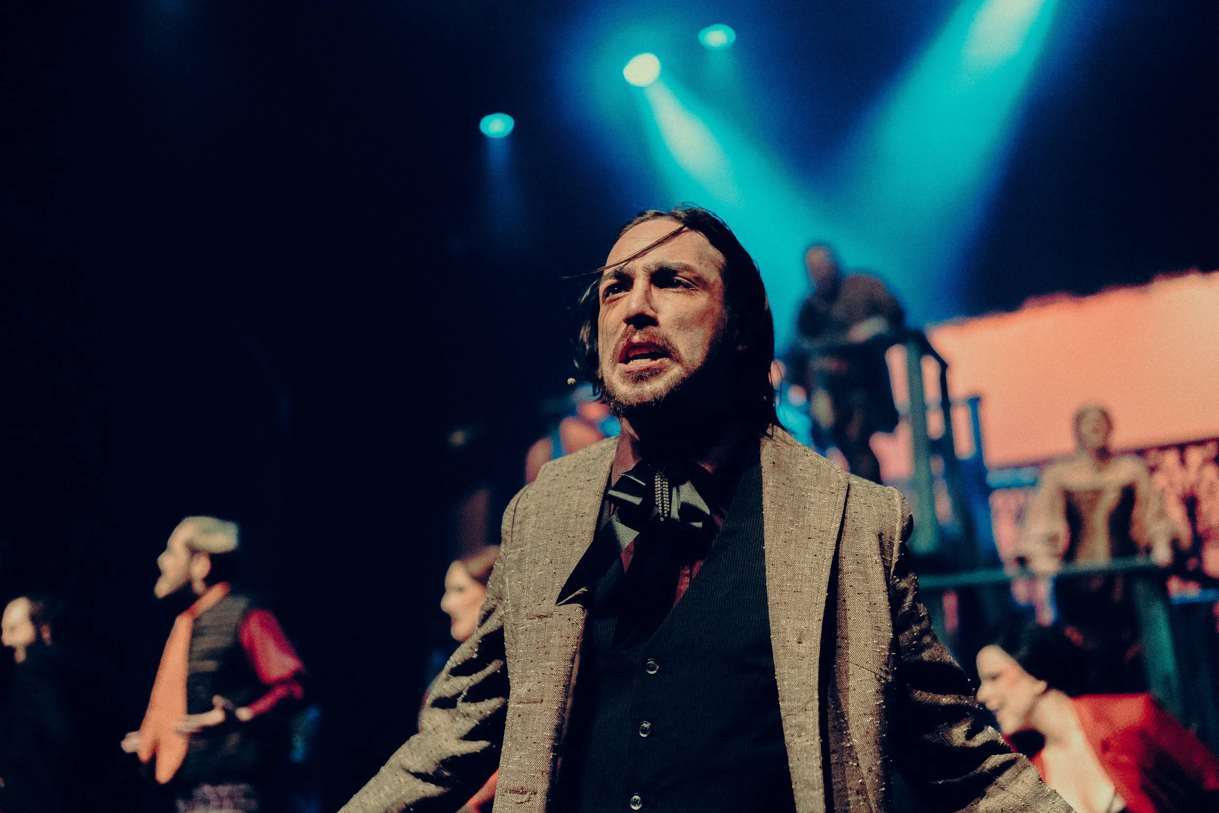 Theatrical performance with actors in period costumes under dramatic lighting on stage.