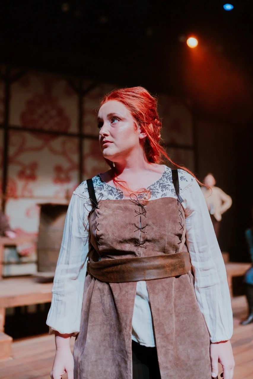 Actor in period costume on stage with dramatic lighting and backdrop, performing in a theater production.