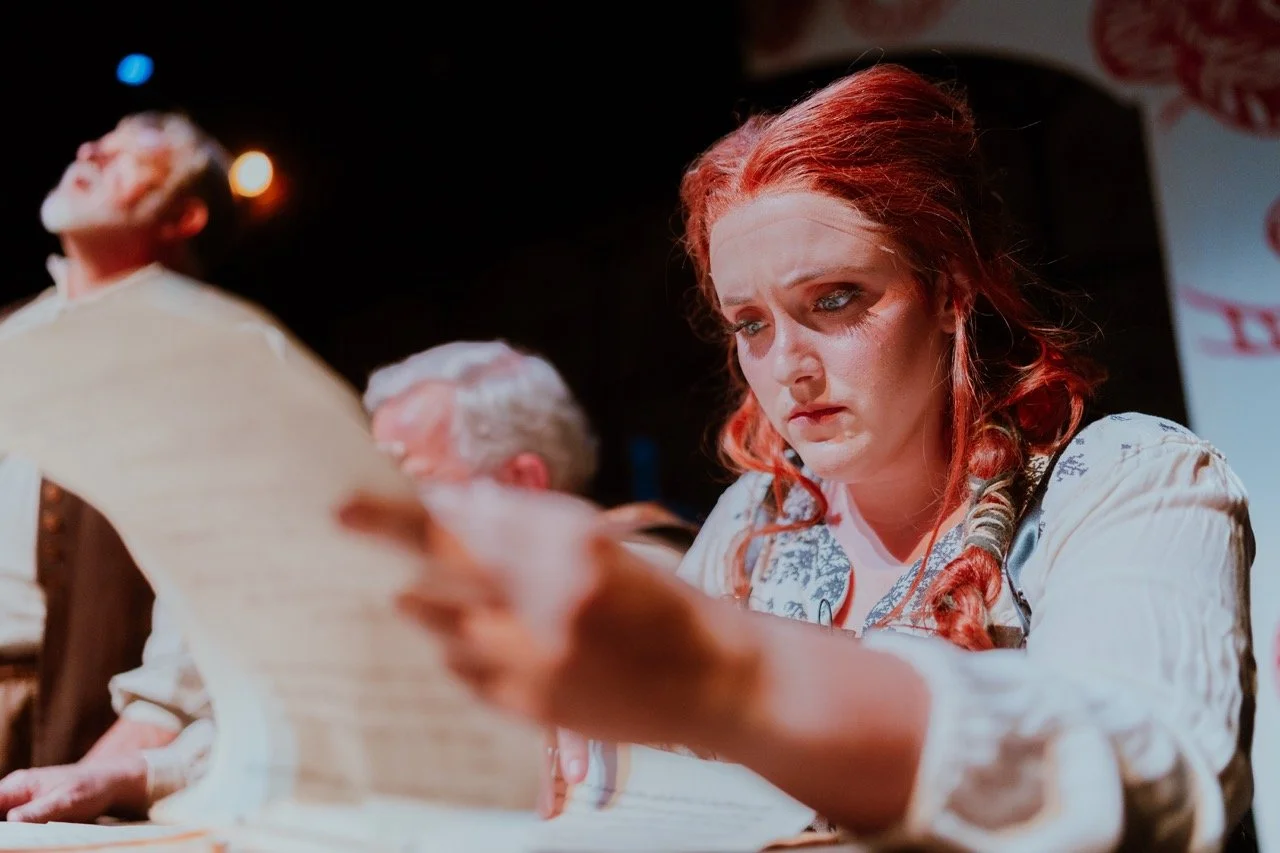 Person dressed in historical costume intensely reading a document during a theatrical performance.