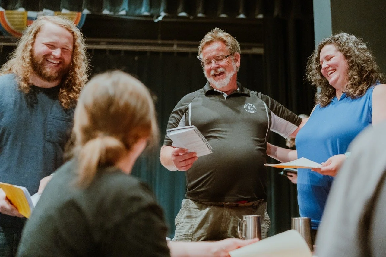 Group of people laughing and holding papers in a casual setting.
