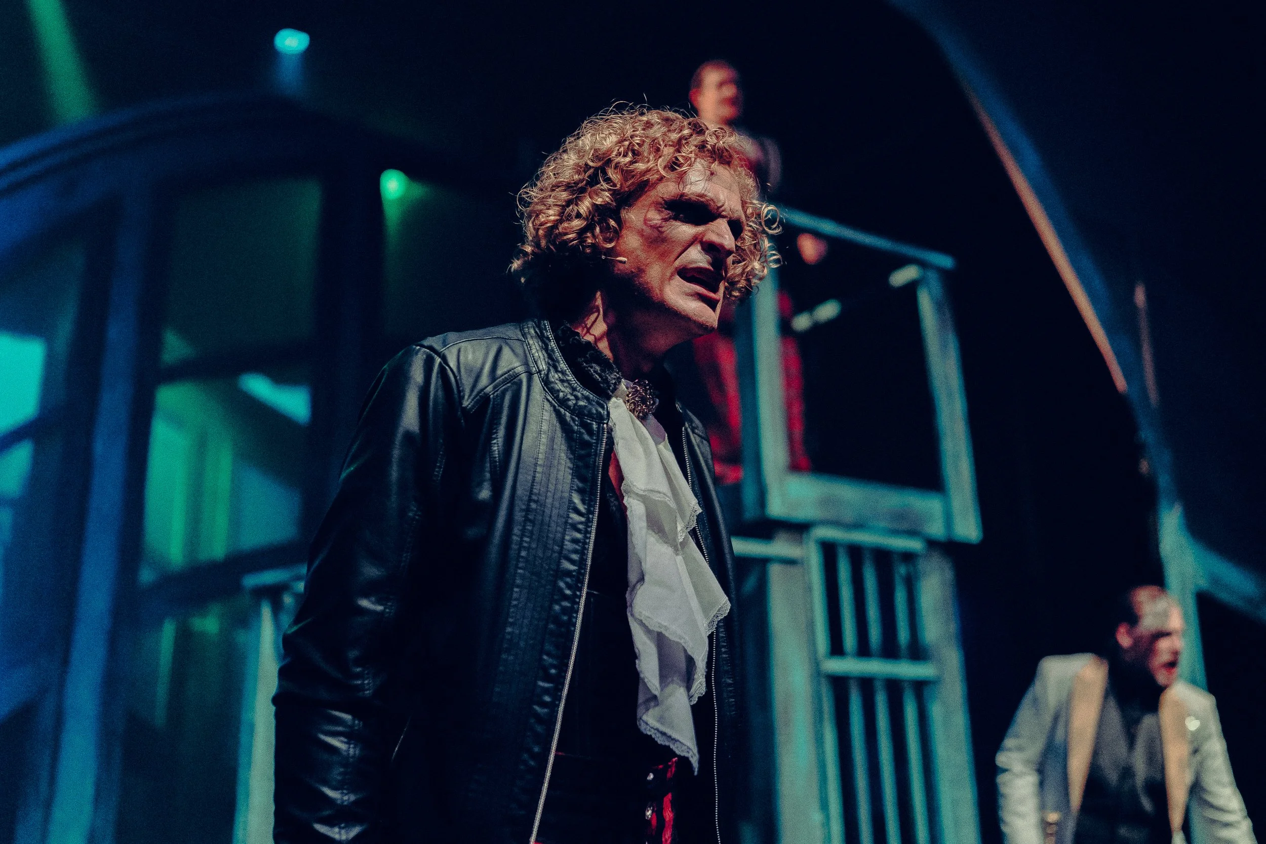 Person in costume on stage performing a dramatic scene with theatrical lighting.