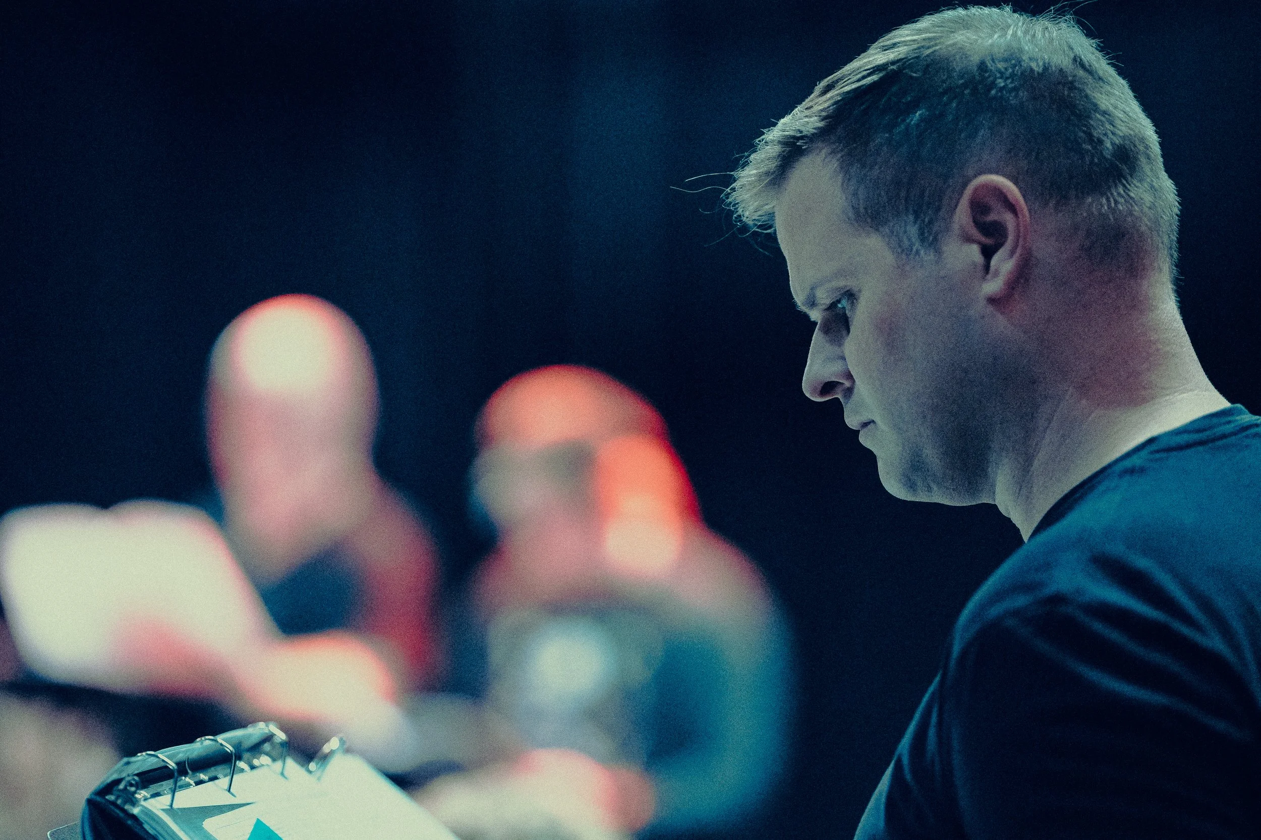 Man focusing on a binder, blurred individuals in background, dark setting