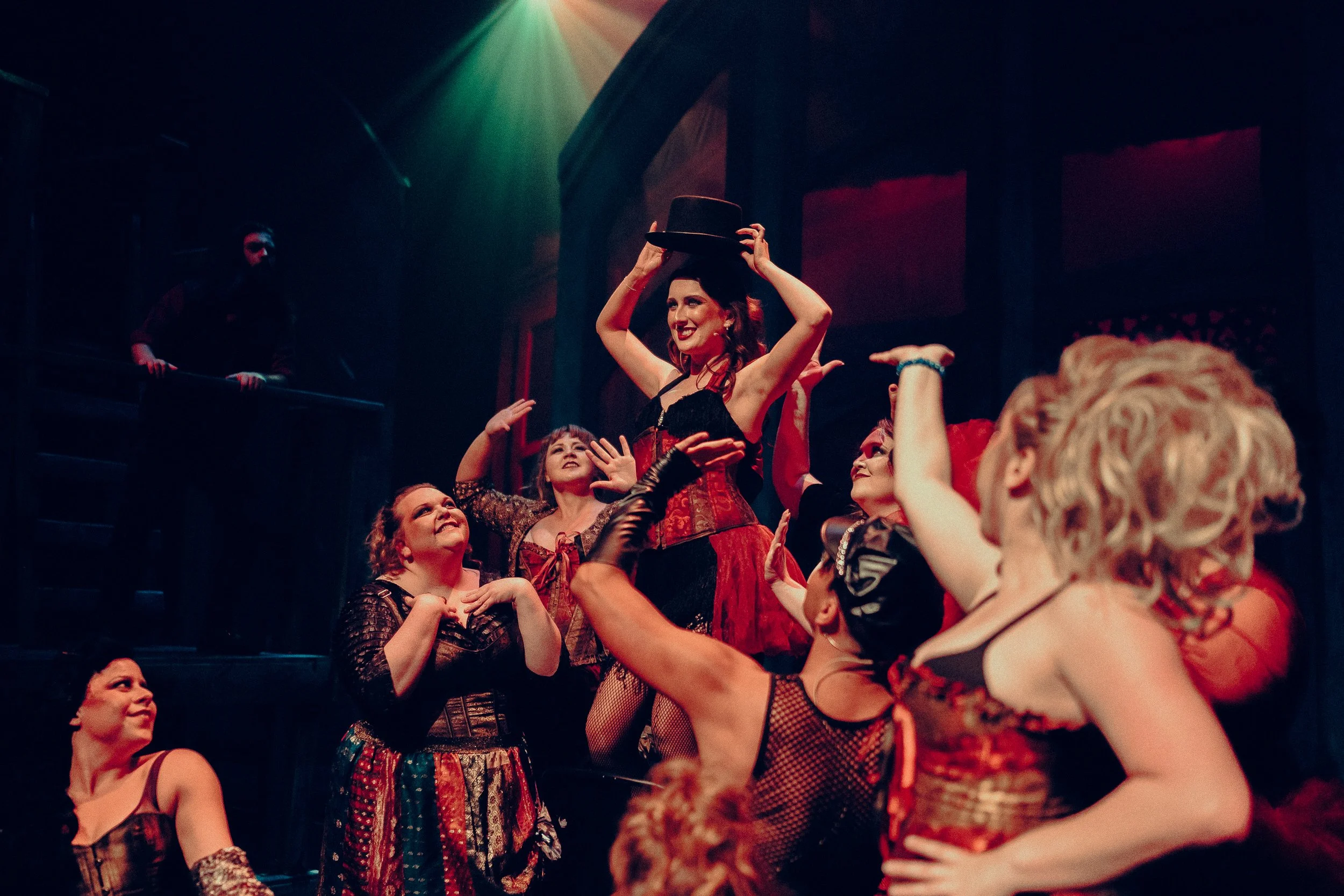 Theater performance with actors in corseted costumes and a woman in a top hat