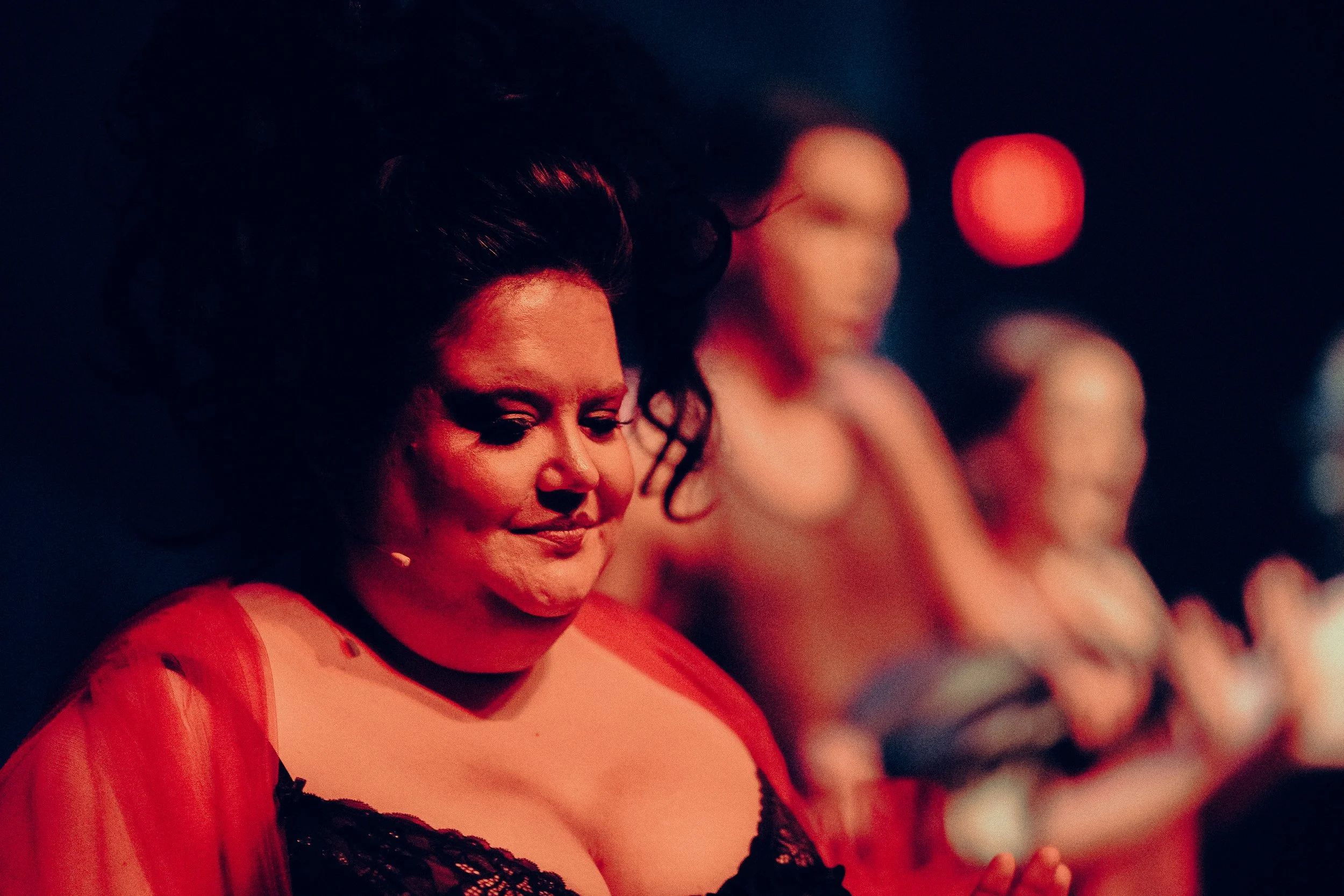 Performer on stage wearing red and black outfit, dramatic makeup, with blurred background.