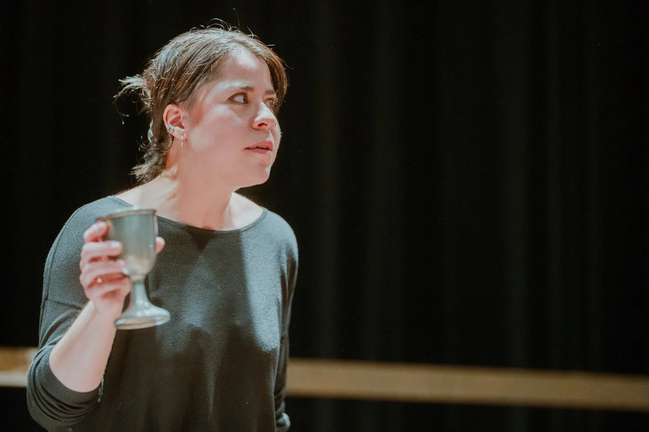 Person holding a silver goblet on stage, black background