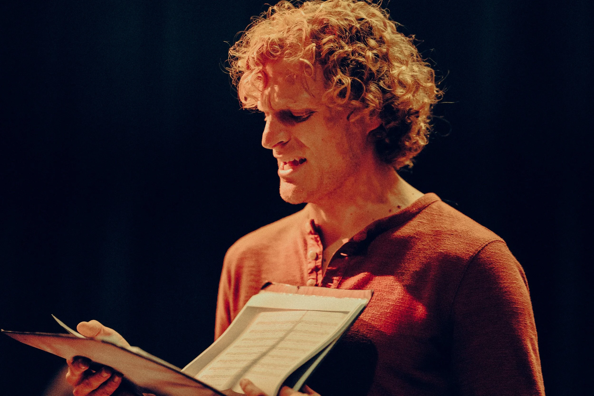 Man with curly hair reading a script on stage