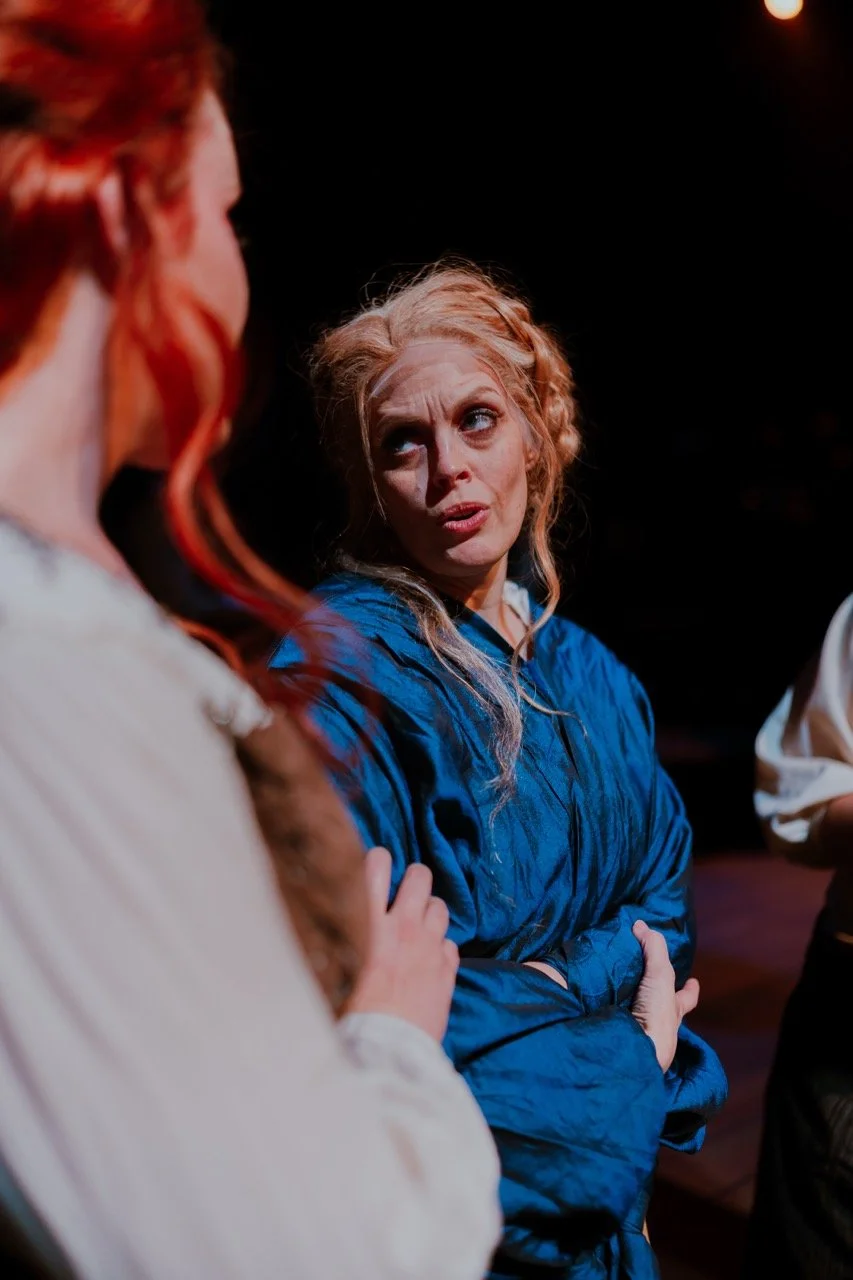 Two women in a dramatic conversation, one wearing a blue robe, in a dimly lit setting.
