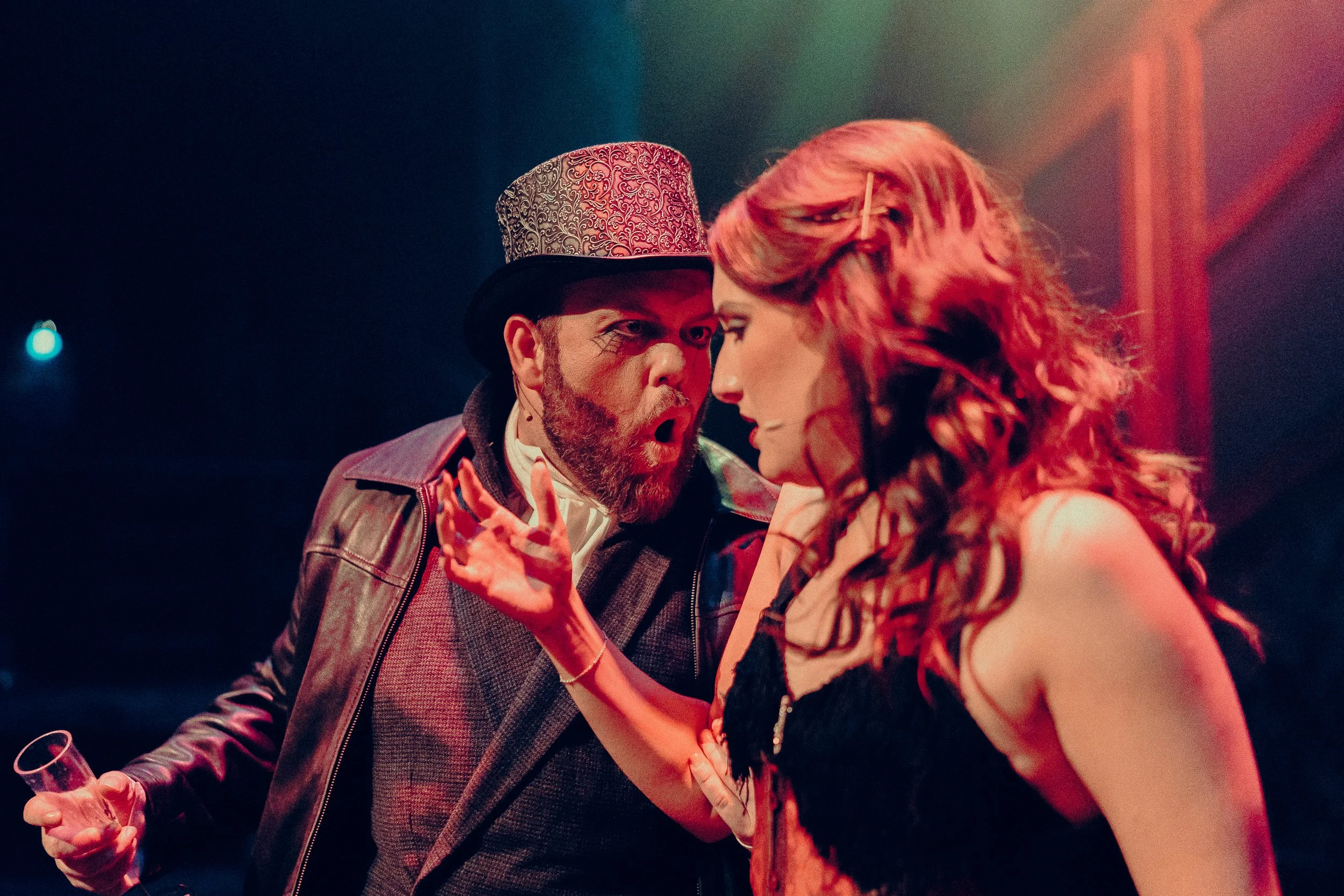 Two actors in dramatic scene on stage, wearing vintage-style costumes with theatrical lighting.