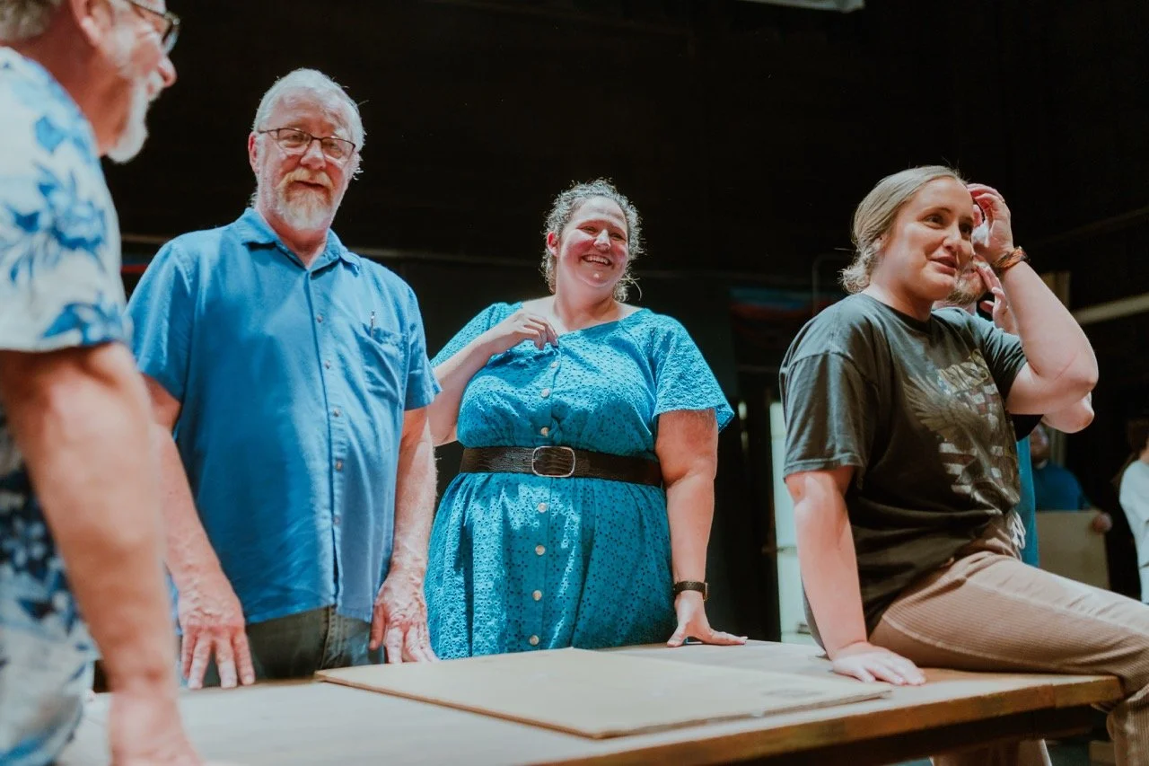 Group of people gathered around a table, casually dressed, engaged in conversation.
