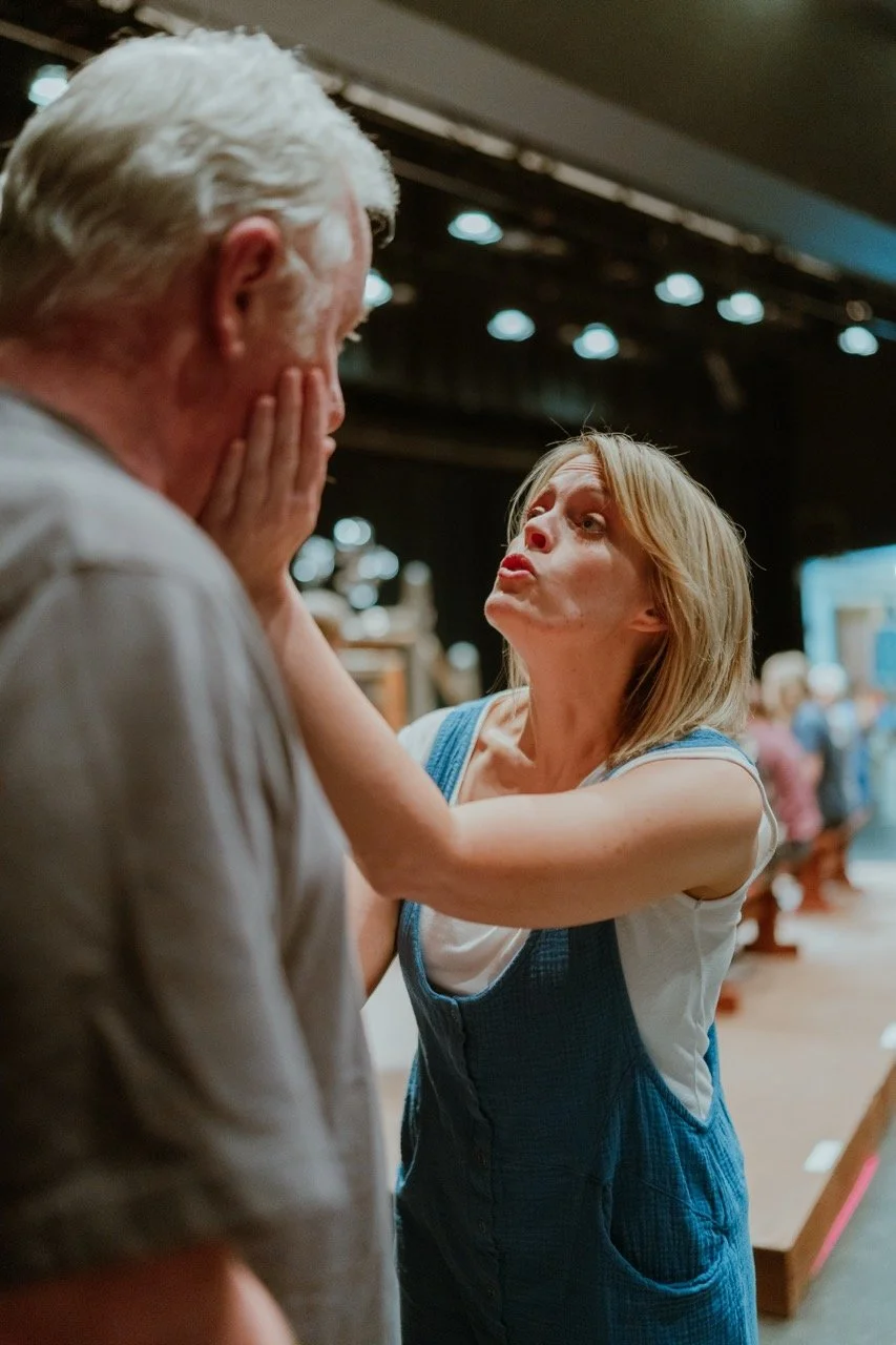 Woman with exaggerated expression holding a man's face on stage.