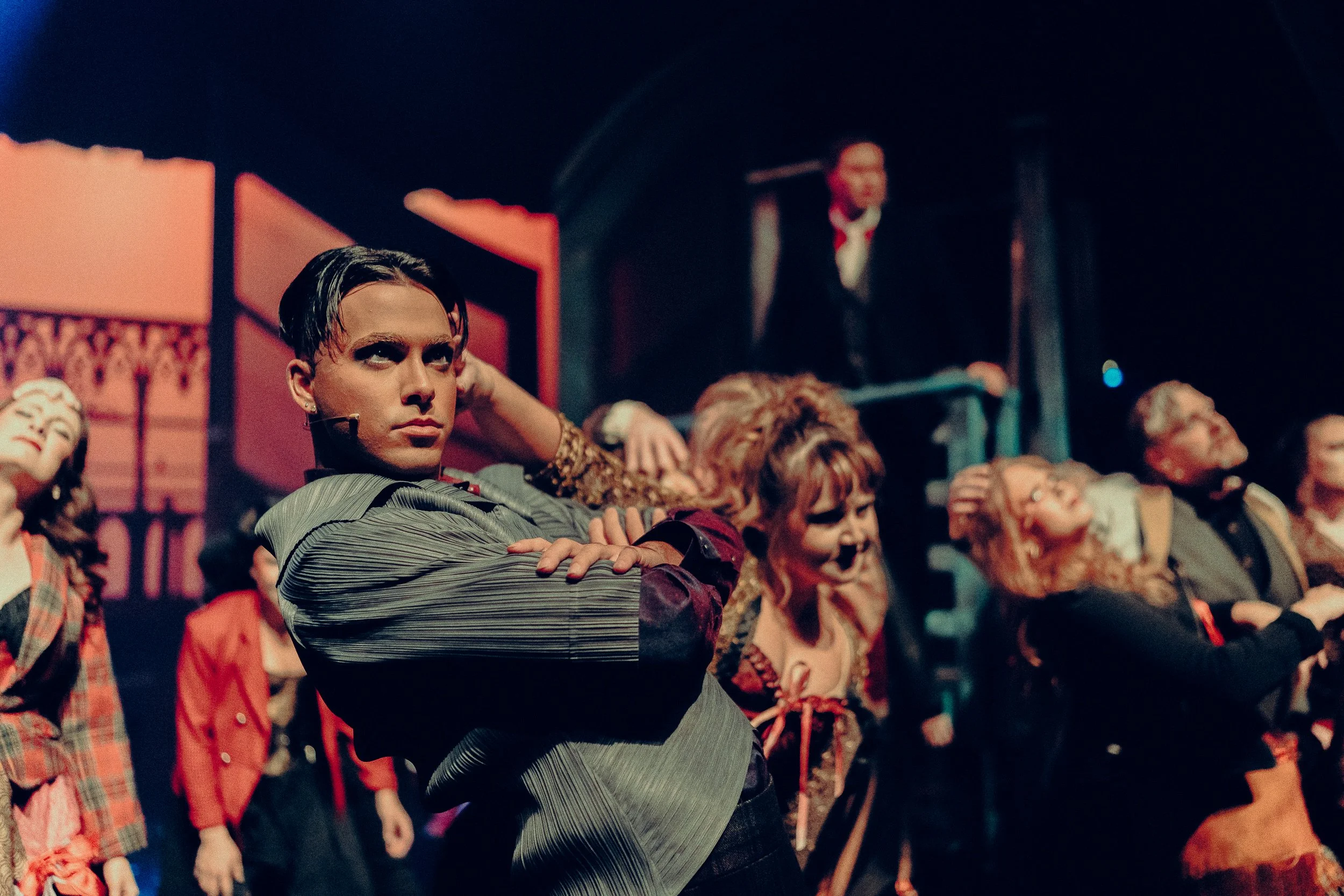 Performers in theatrical costumes on stage with dramatic poses and colorful lighting.