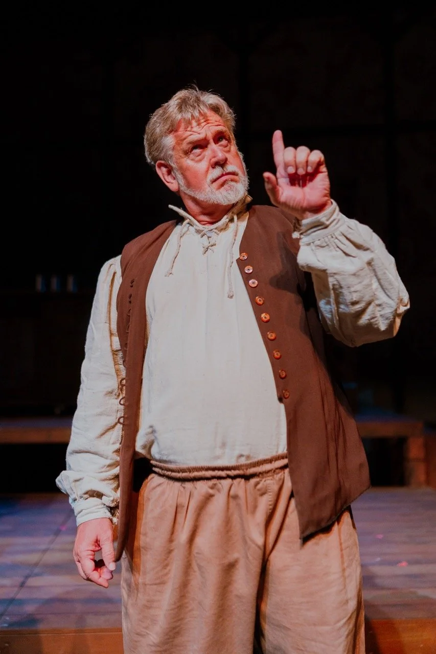 Man in historical clothing performing on stage with dramatic gesture.