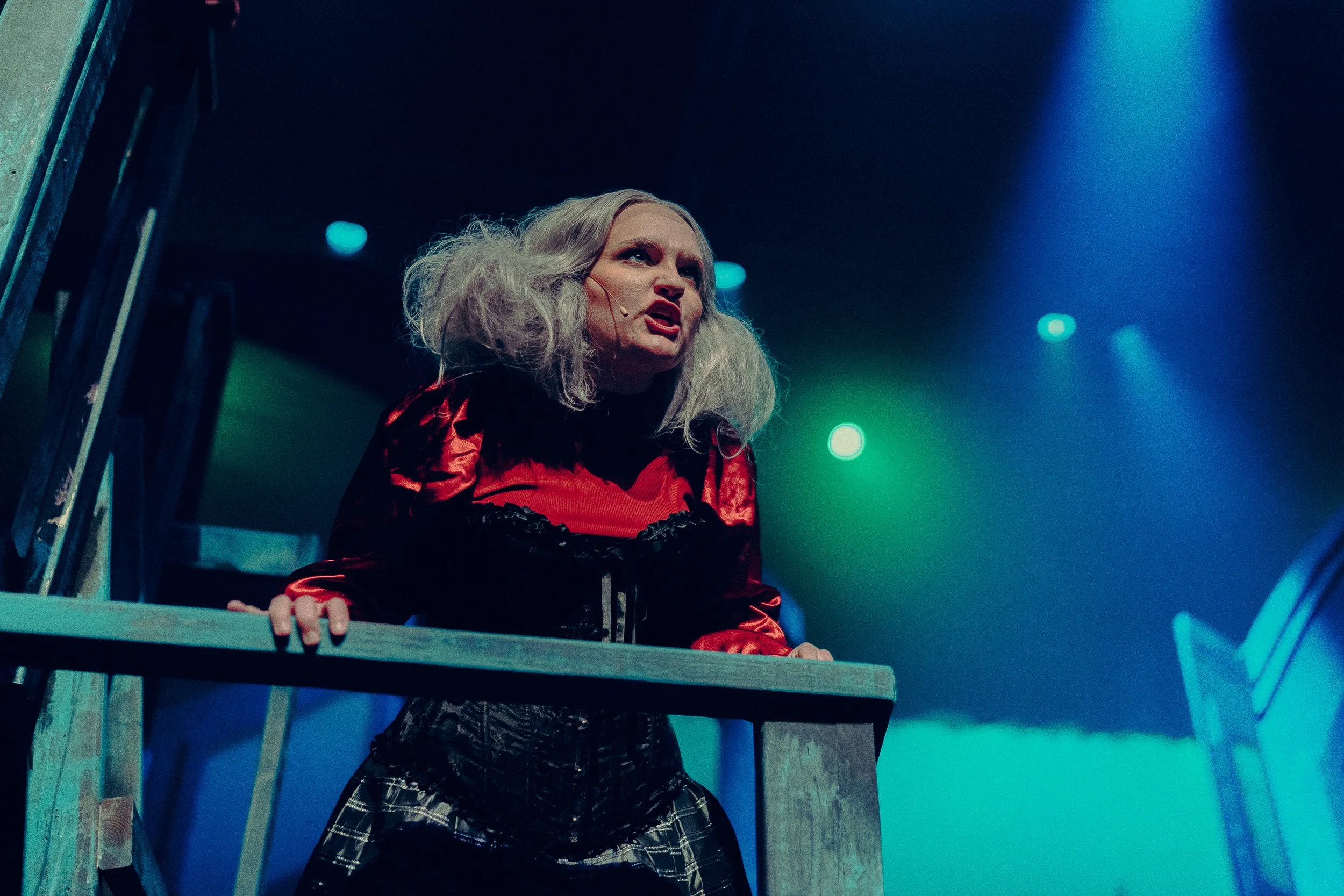 Performer in theatrical costume with white hair and red gown on stage.