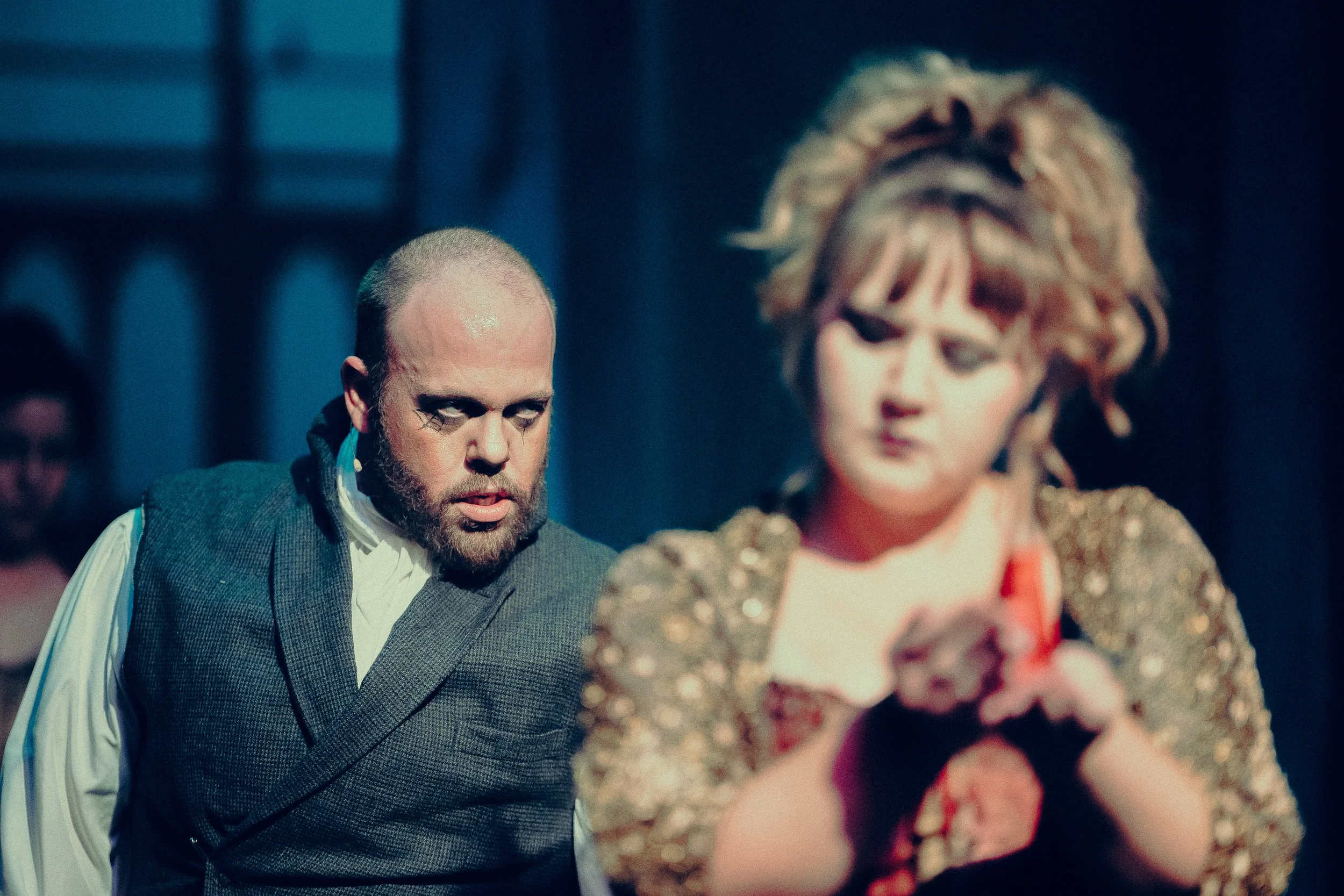 Two people in dramatic theatrical costumes with intense expressions, suggesting a performance on stage.