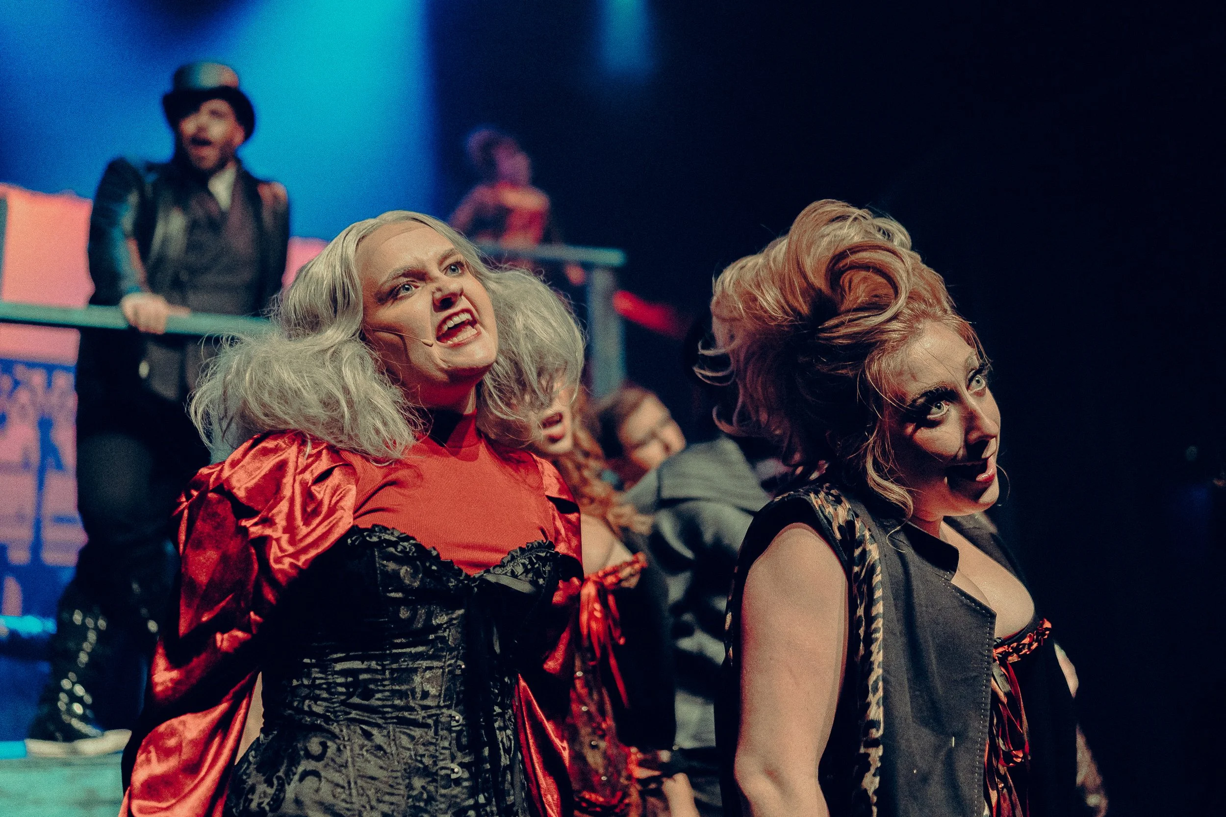 Theater performance with actors in dramatic costumes on stage, featuring vibrant lighting and expressive poses.