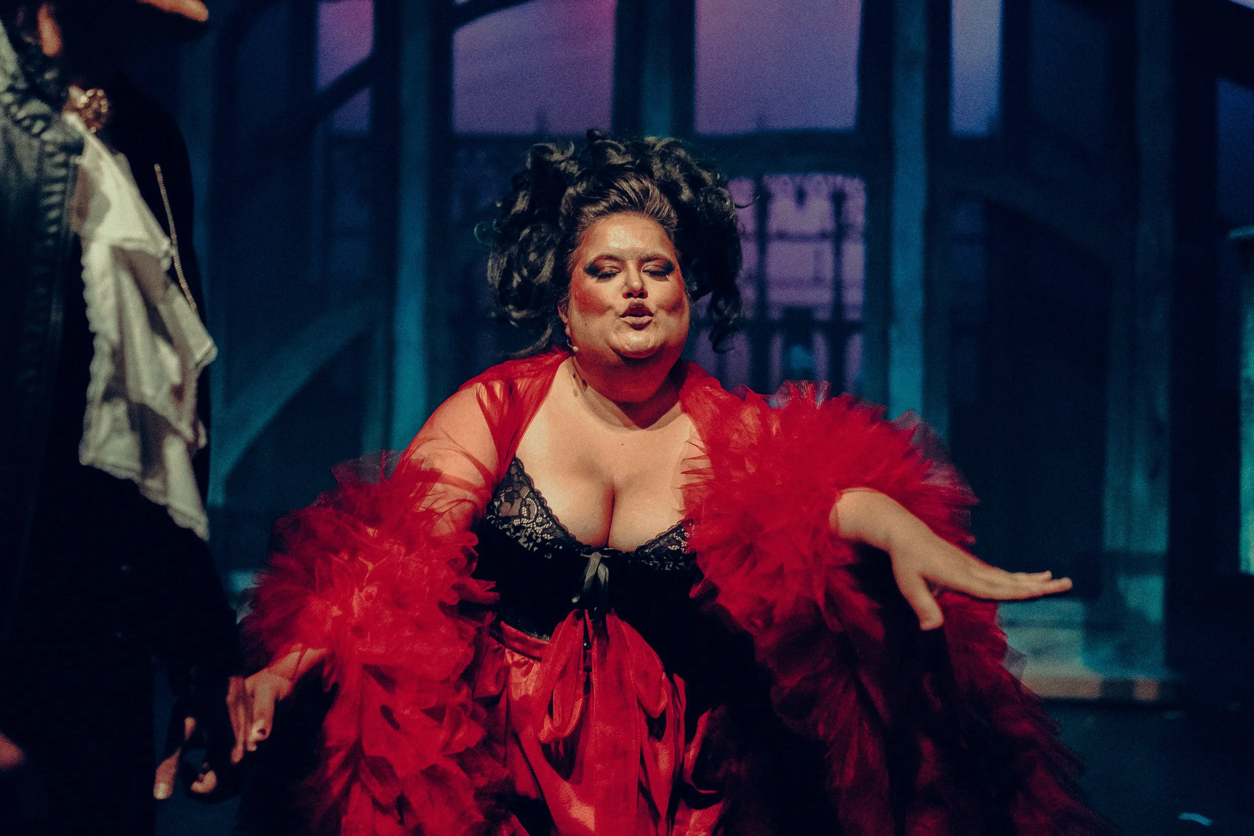 Person performing on stage in dramatic red and black costume with bold makeup.