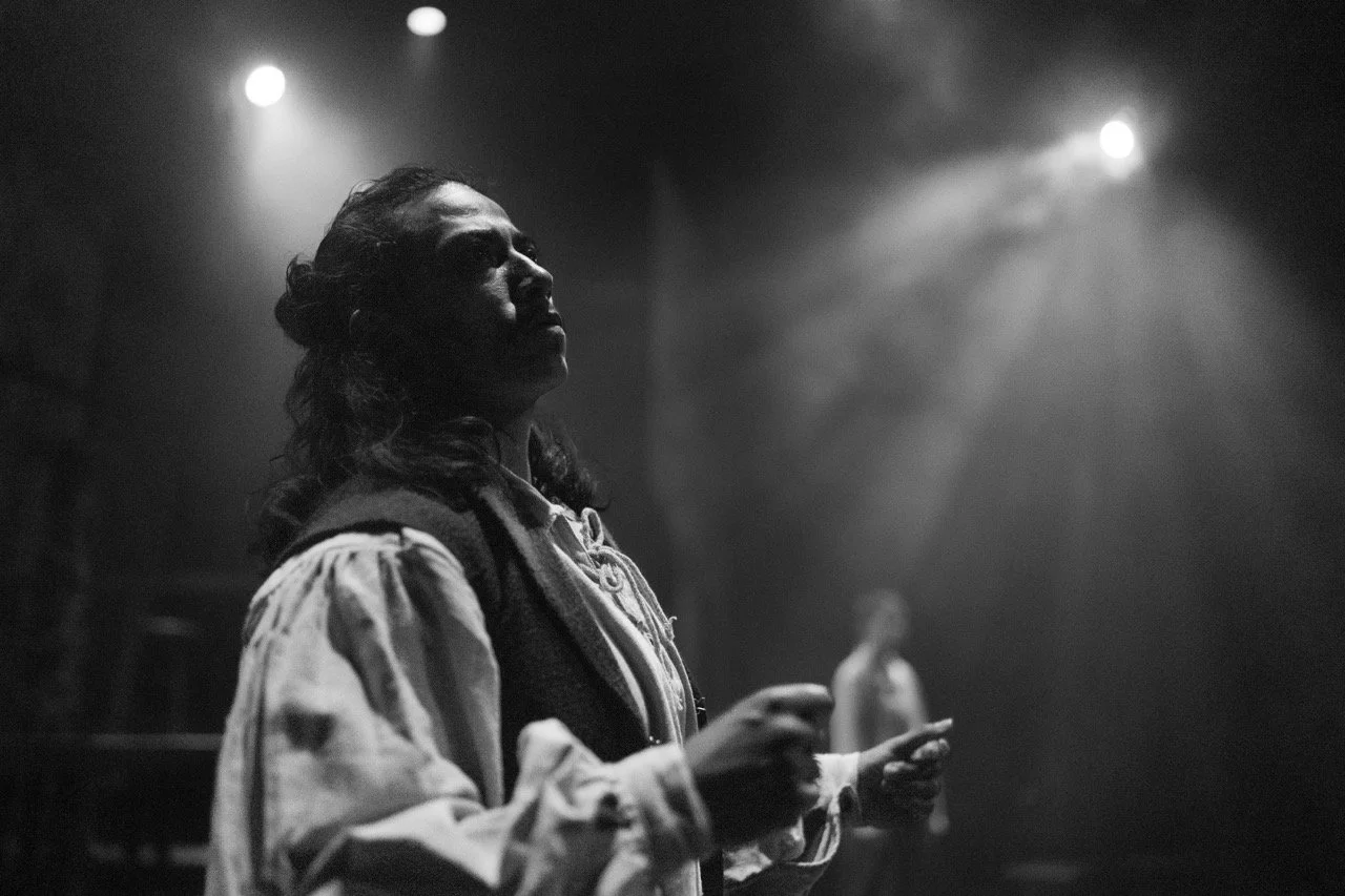 Black and white photo of a person in historical costume on stage, dramatic lighting.