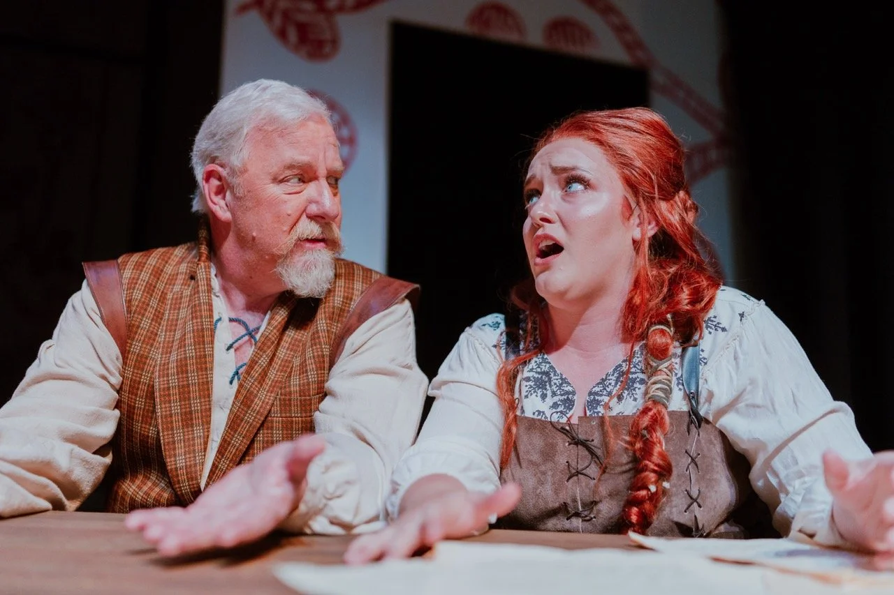 Two actors in period costumes engaged in an intense conversation on stage.