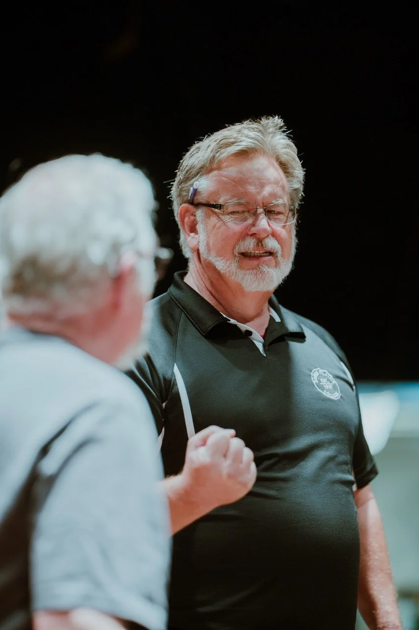 Two men conversing, one in a black polo shirt.