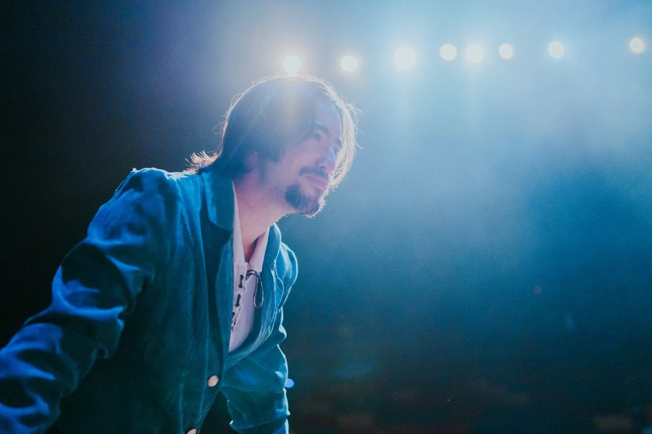 Person in a blue jacket under stage lights, looking forward with a slight smile.