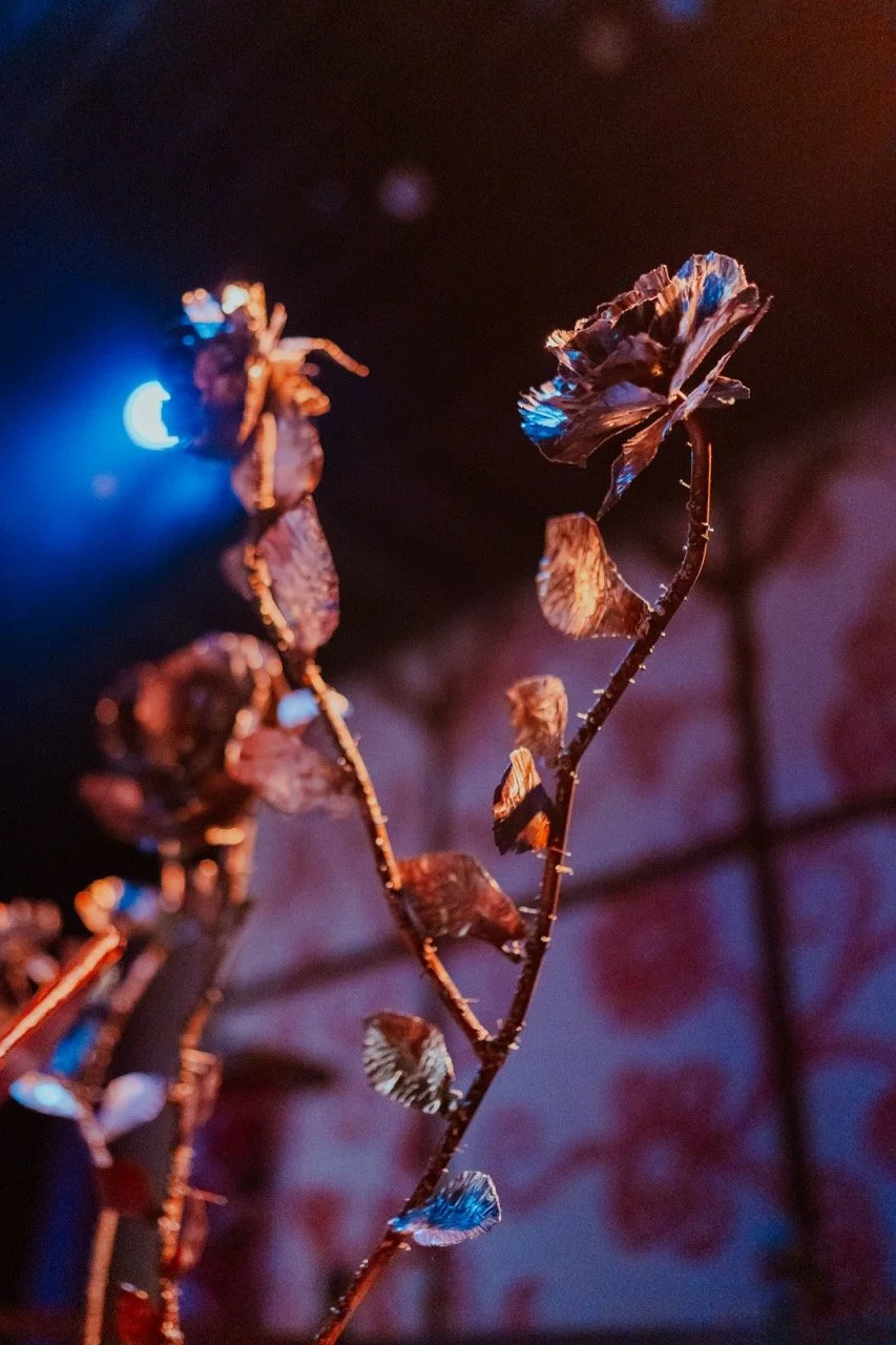 Metallic flower sculpture with blue and orange lighting against a blurred background.