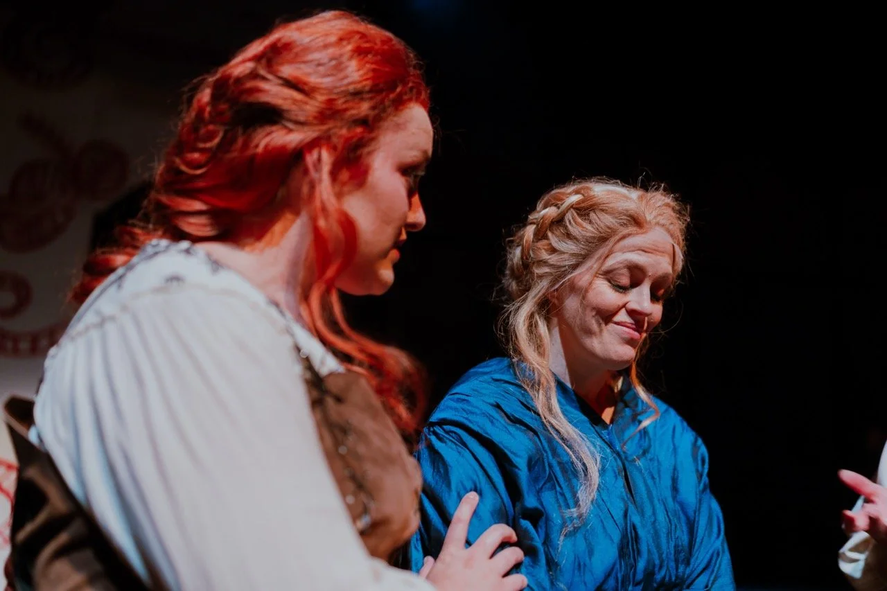 Two women with braided hairstyles in historical costumes performing on stage.