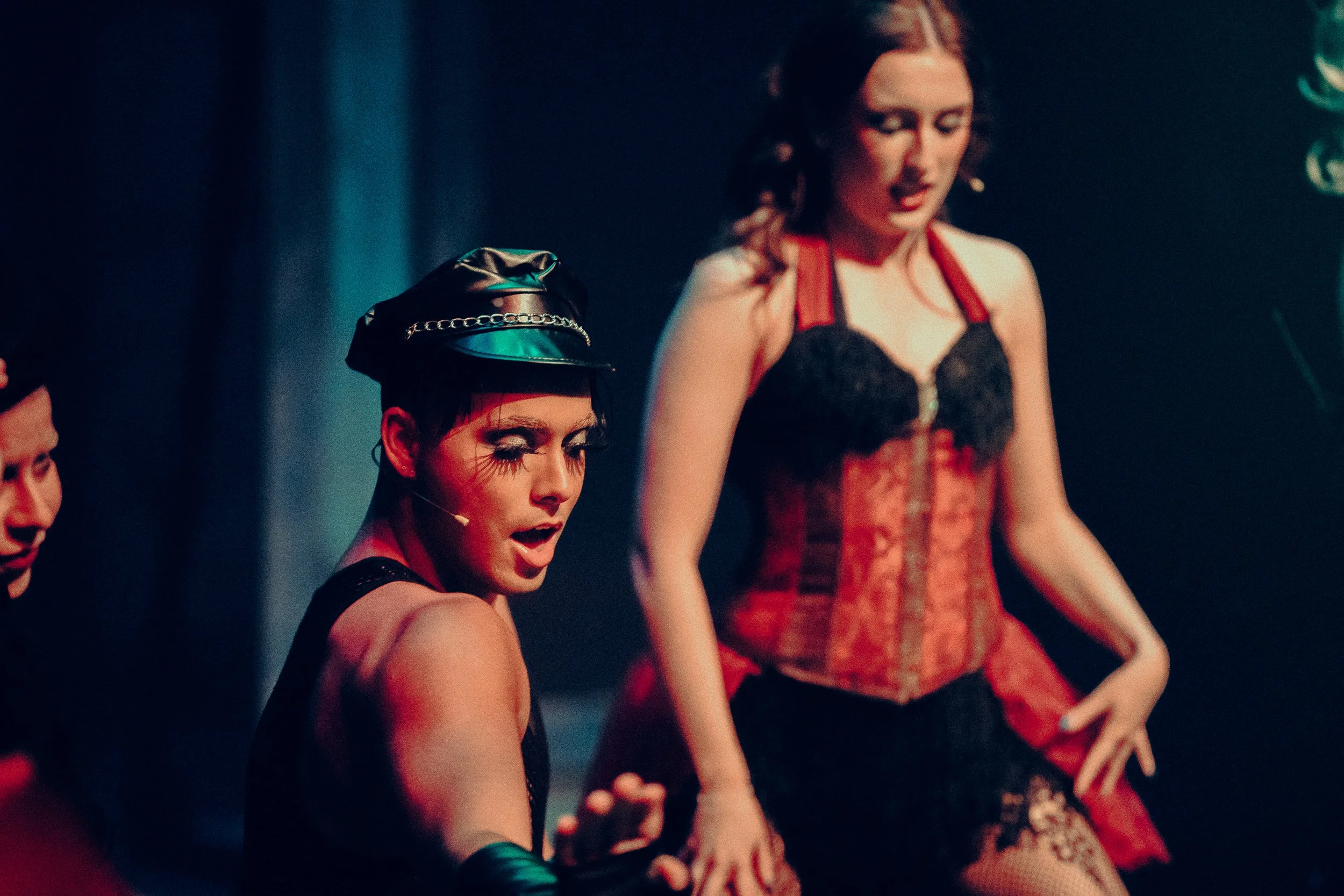 Performers in theatrical costumes on stage with dramatic makeup and lighting.