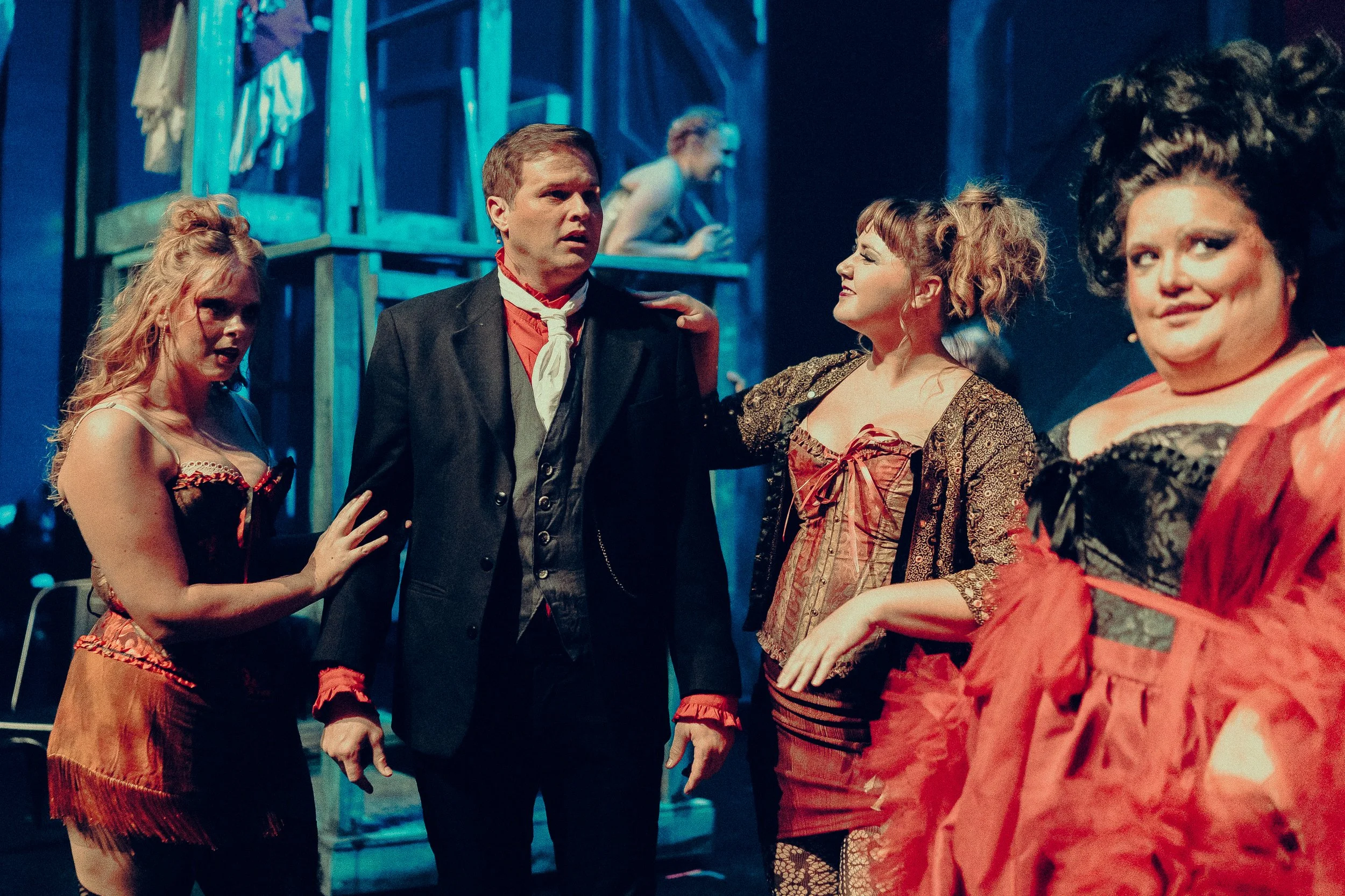 Four people in theatrical costumes on stage, with a blue-toned set in the background.