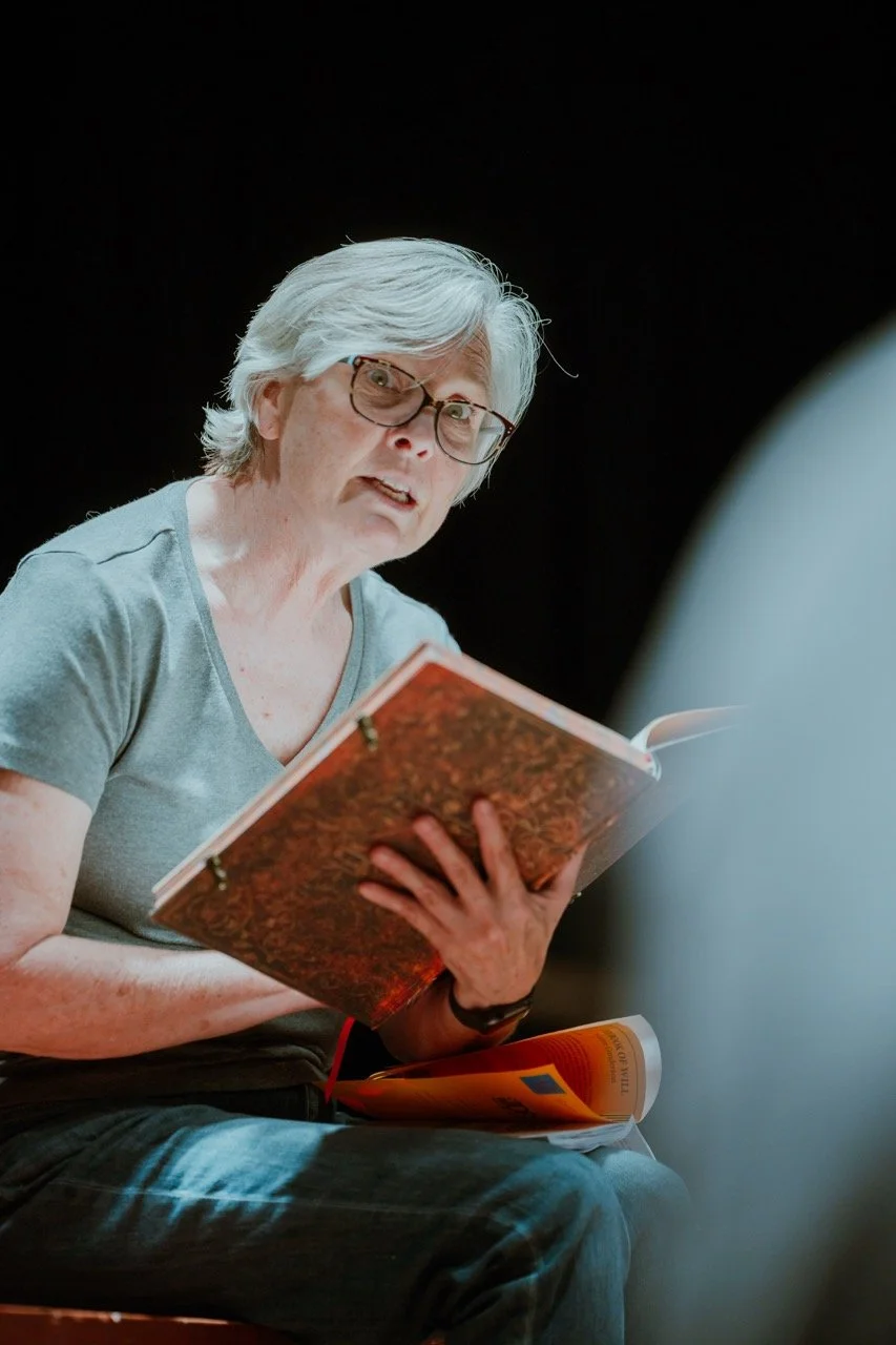 Older person with glasses reading from a book in a dark room.