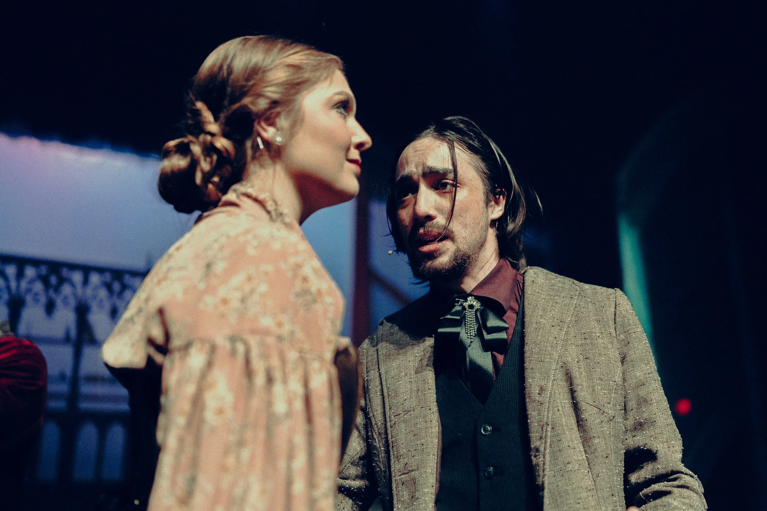 Two actors performing on stage in vintage costumes with dramatic expressions, dim lighting.