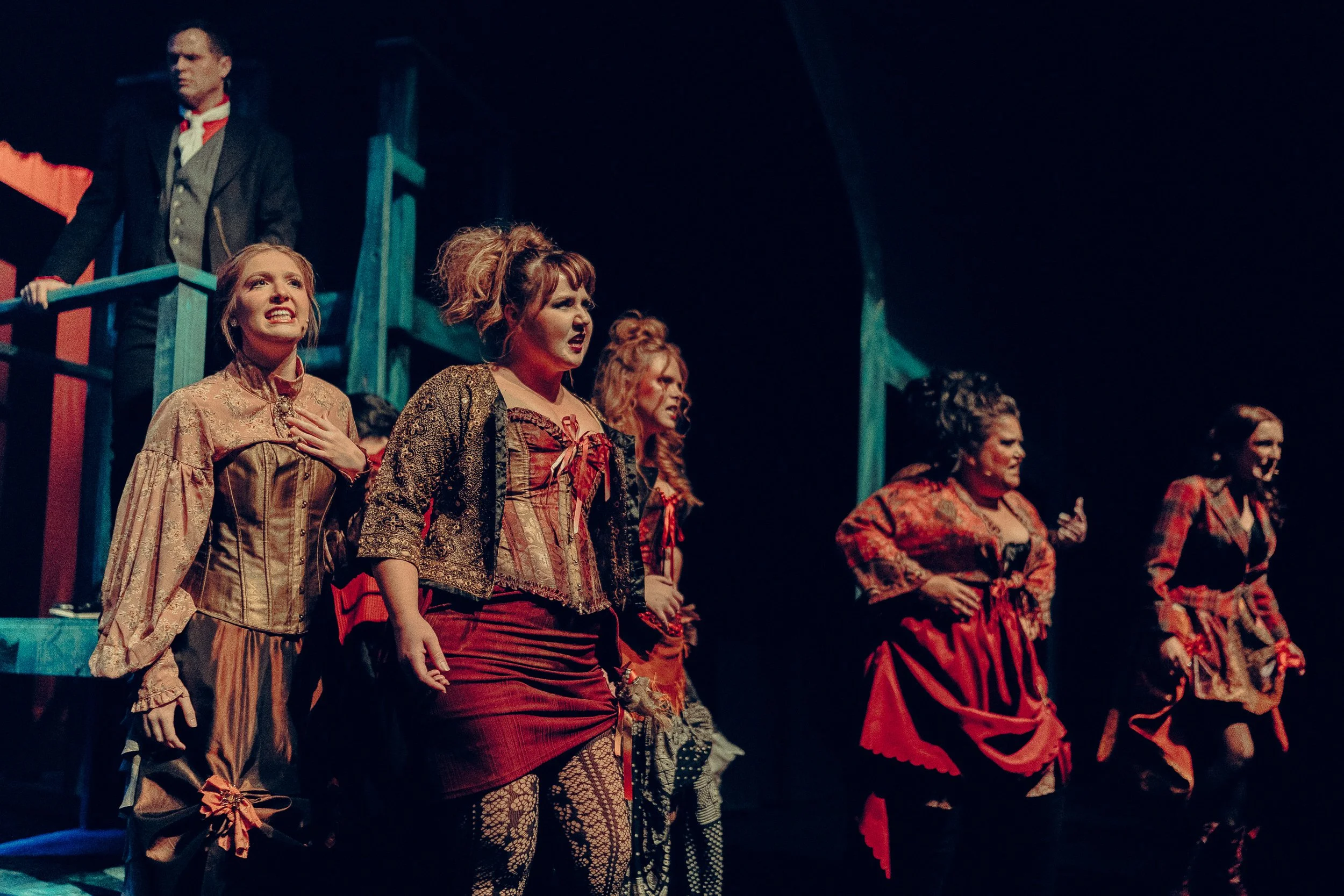 Group of performers on stage in period costumes during a theatrical performance.