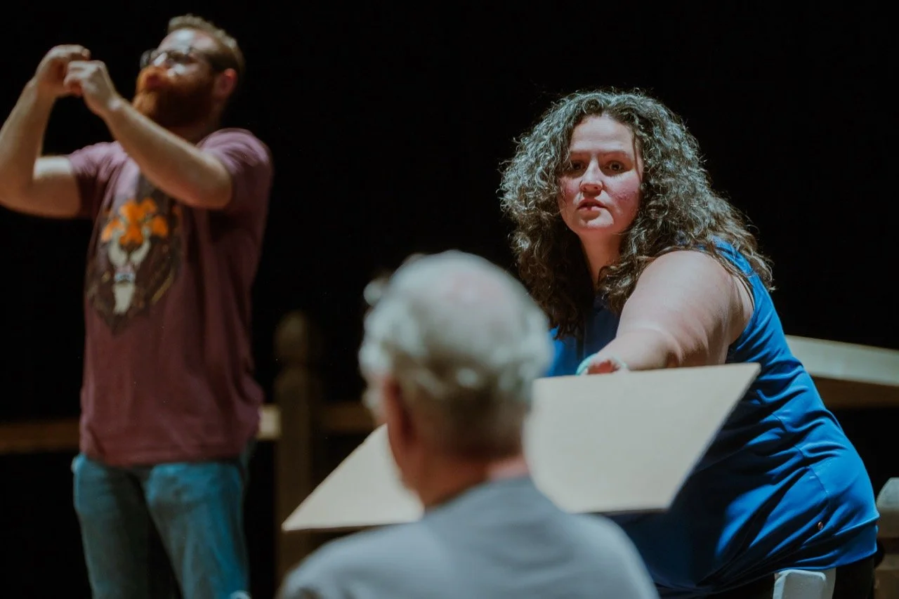 Three people interacting in a dimly lit setting, with one woman holding a piece of paper.