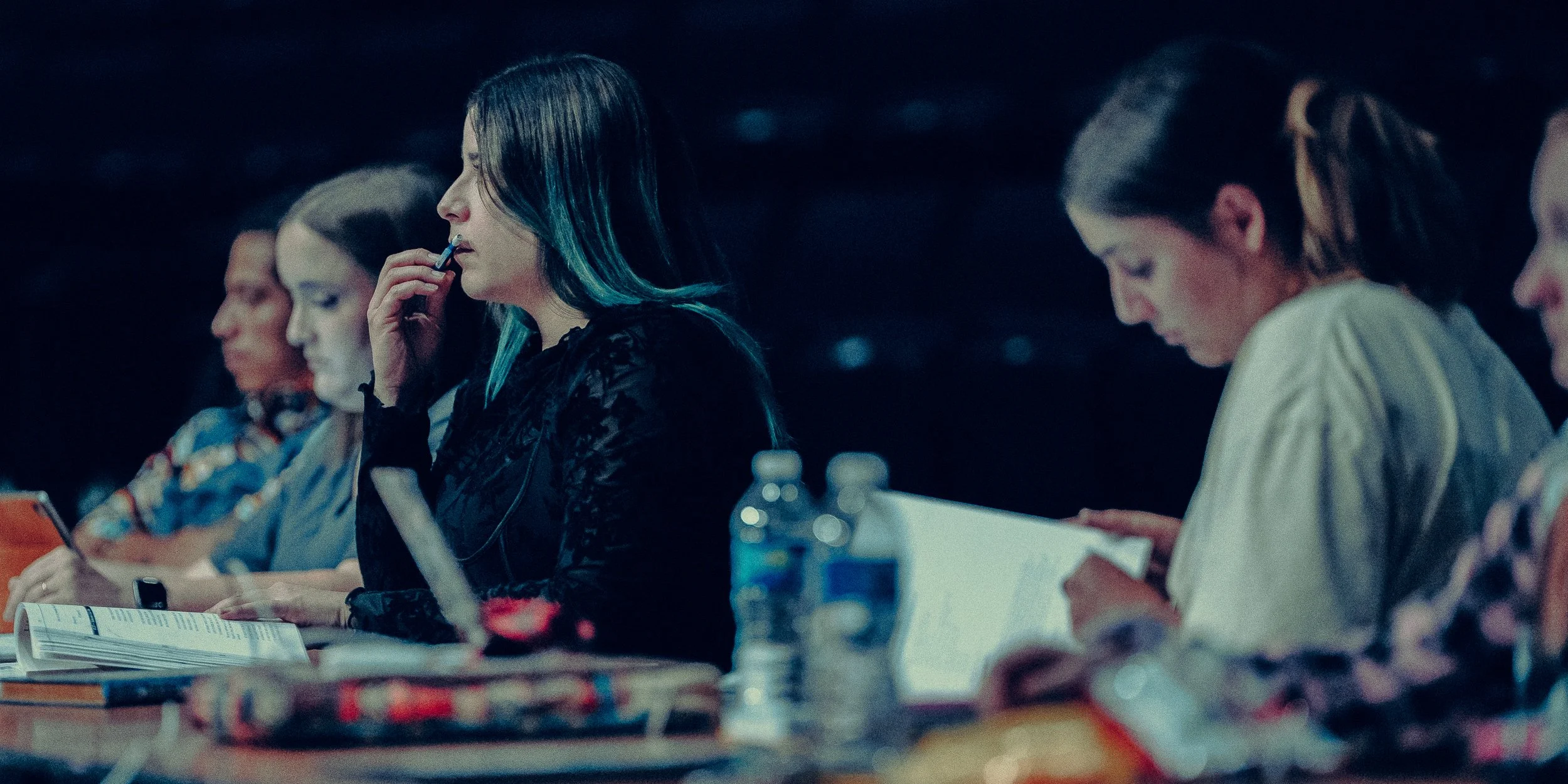Several people sitting at a table, reading and taking notes, with water bottles present.