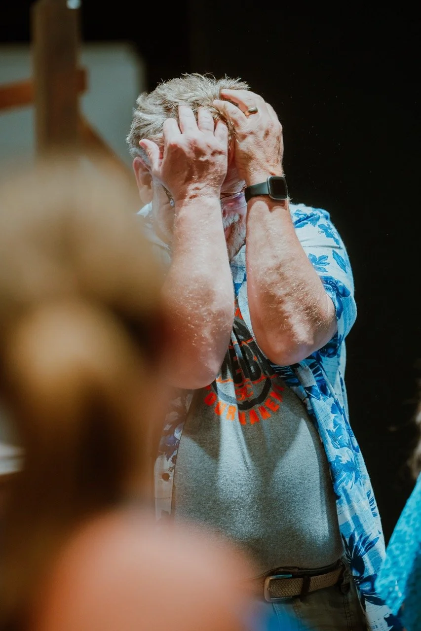 Person in a blue Hawaiian shirt holding their head with both hands, appearing stressed, with a blurred foreground.