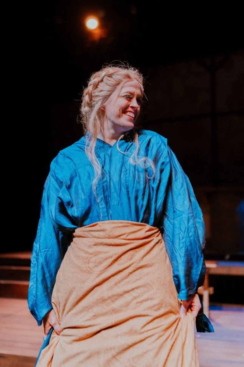 Woman in blue dress and beige wrap performing on stage with spotlight in background.