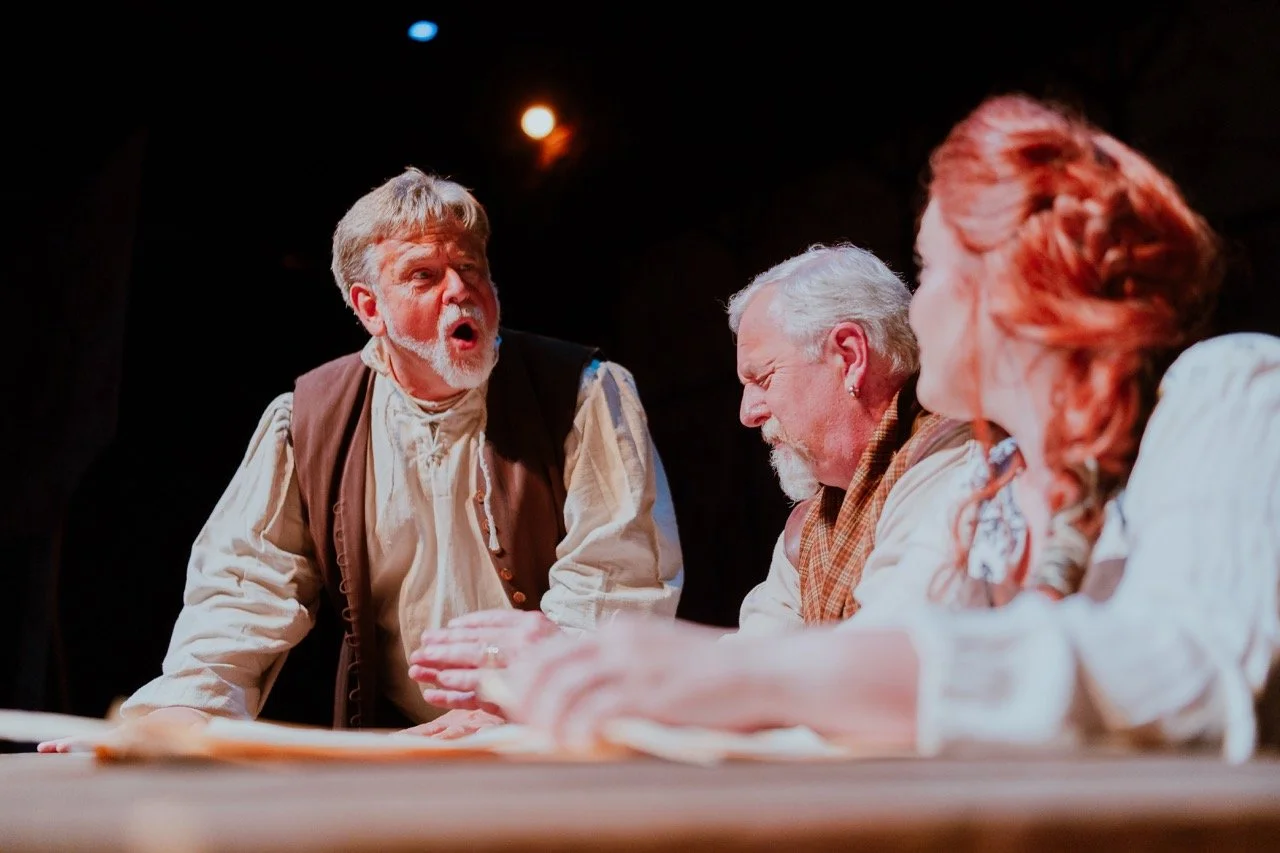 Three actors in a theatrical performance, dressed in historical costumes, engaged in an intense scene with expressive gestures.