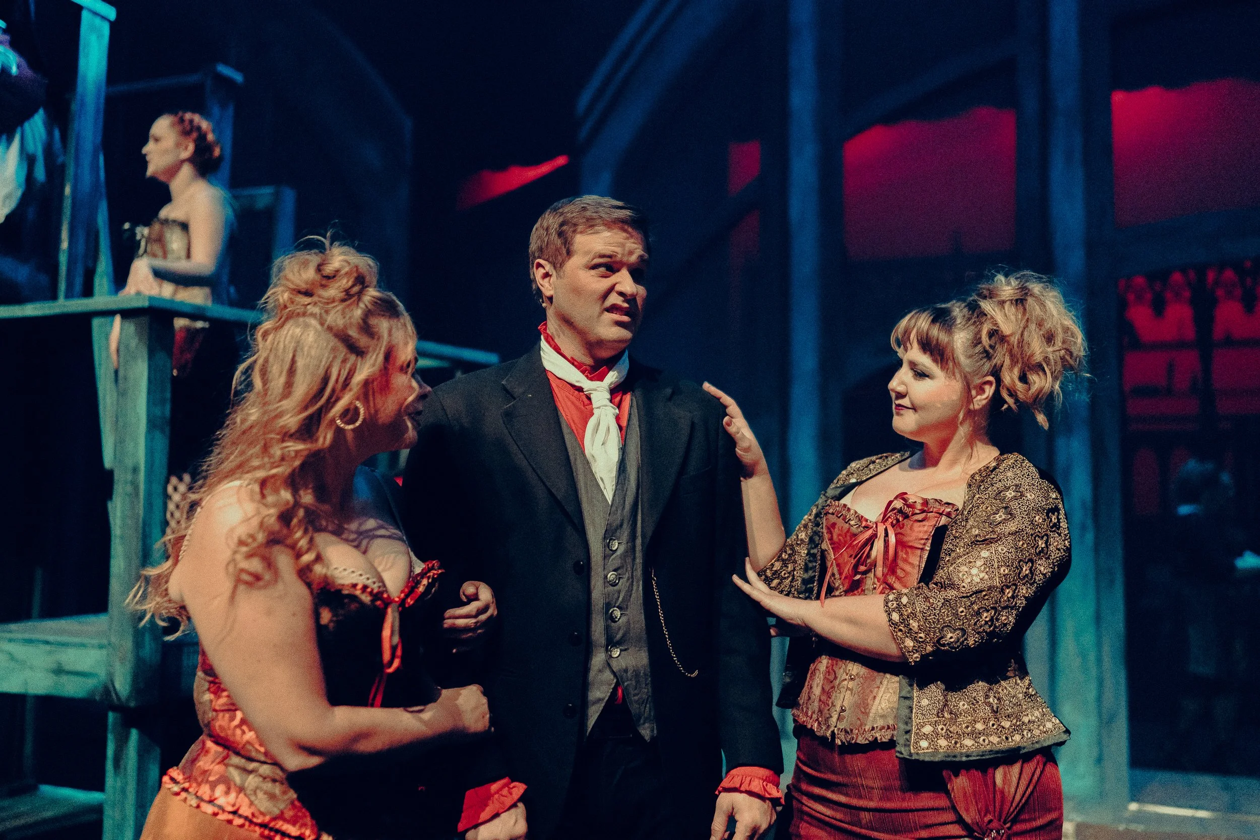 Three people in theatrical Victorian costumes performing on stage with dramatic lighting.
