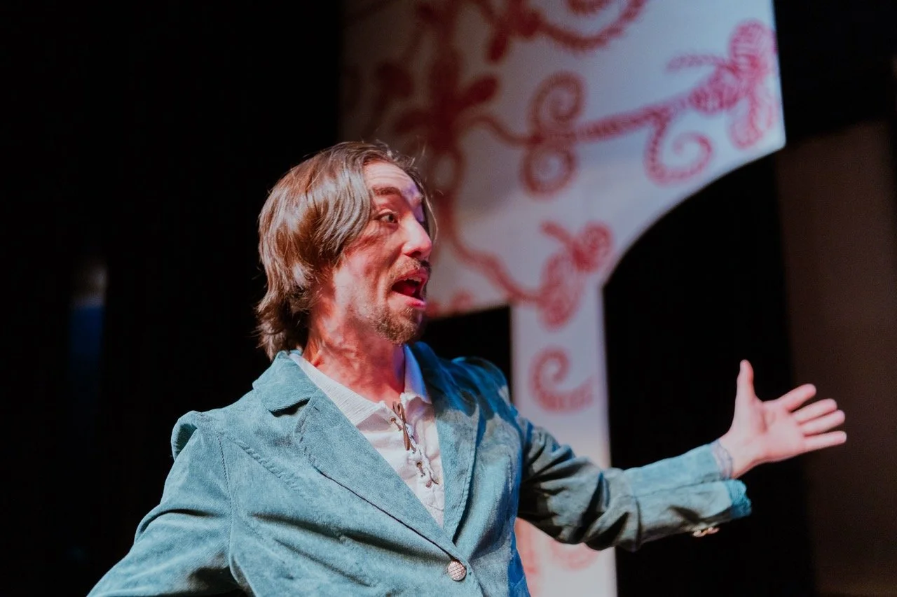 Man in blue suit performing on stage with expressive gesture, abstract red and white background.
