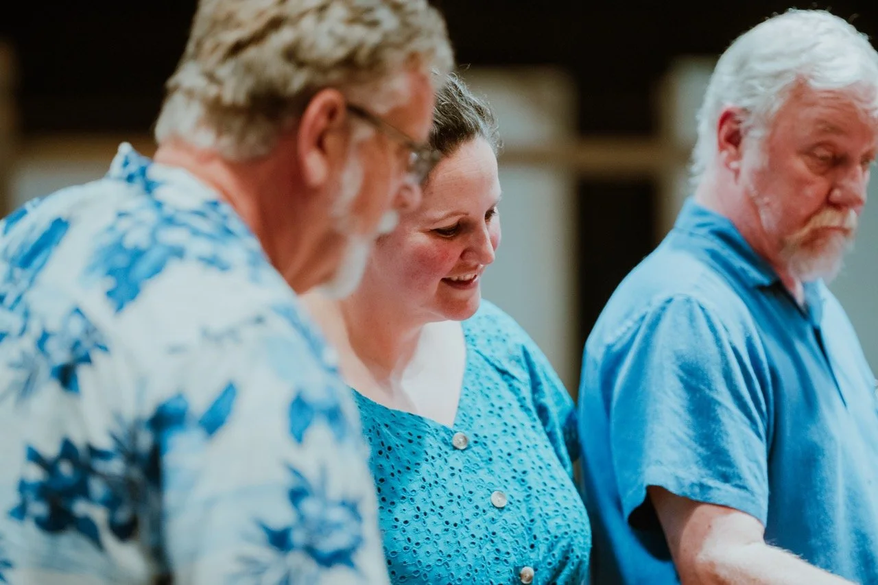 Three people standing close together, wearing blue-patterned shirts, with one person smiling.