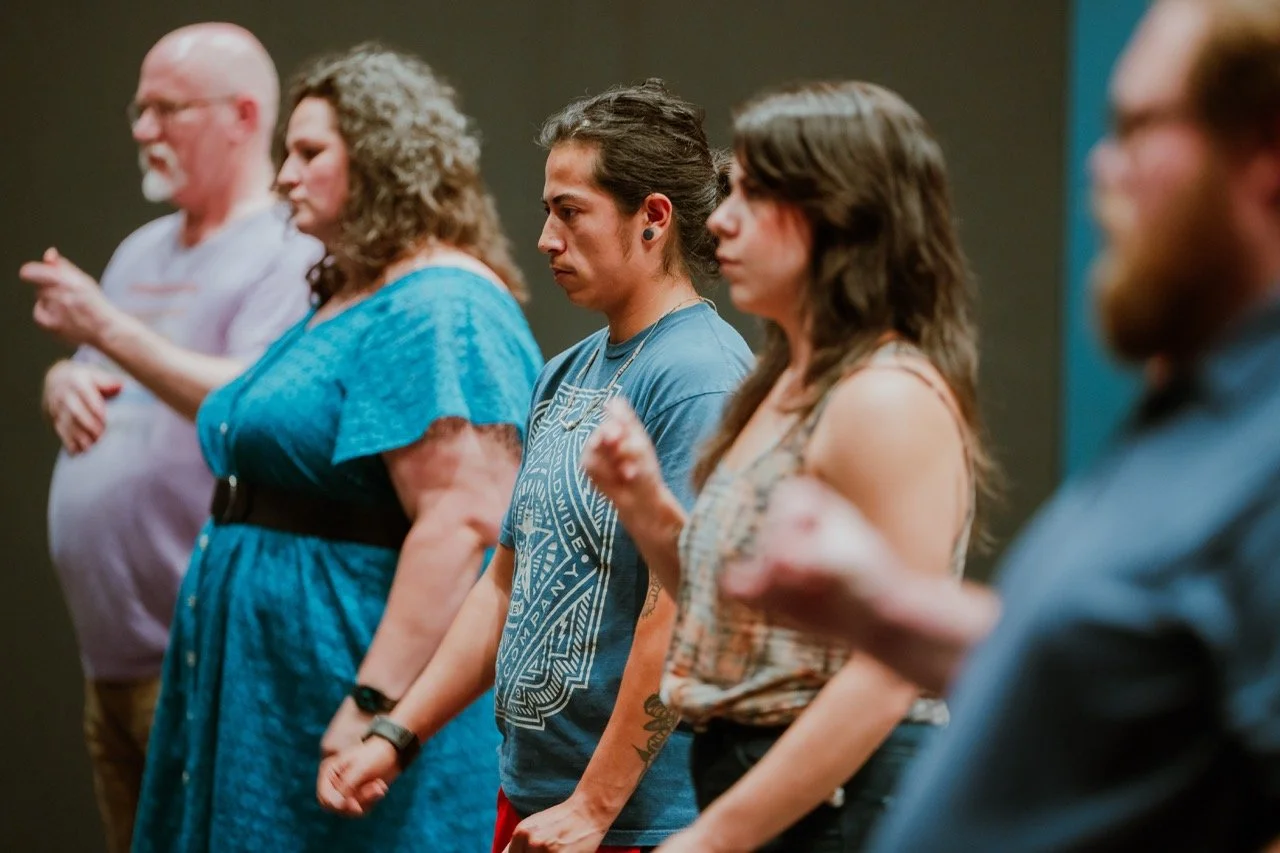 Group of people standing in a line, focused on something off-camera, indoors.