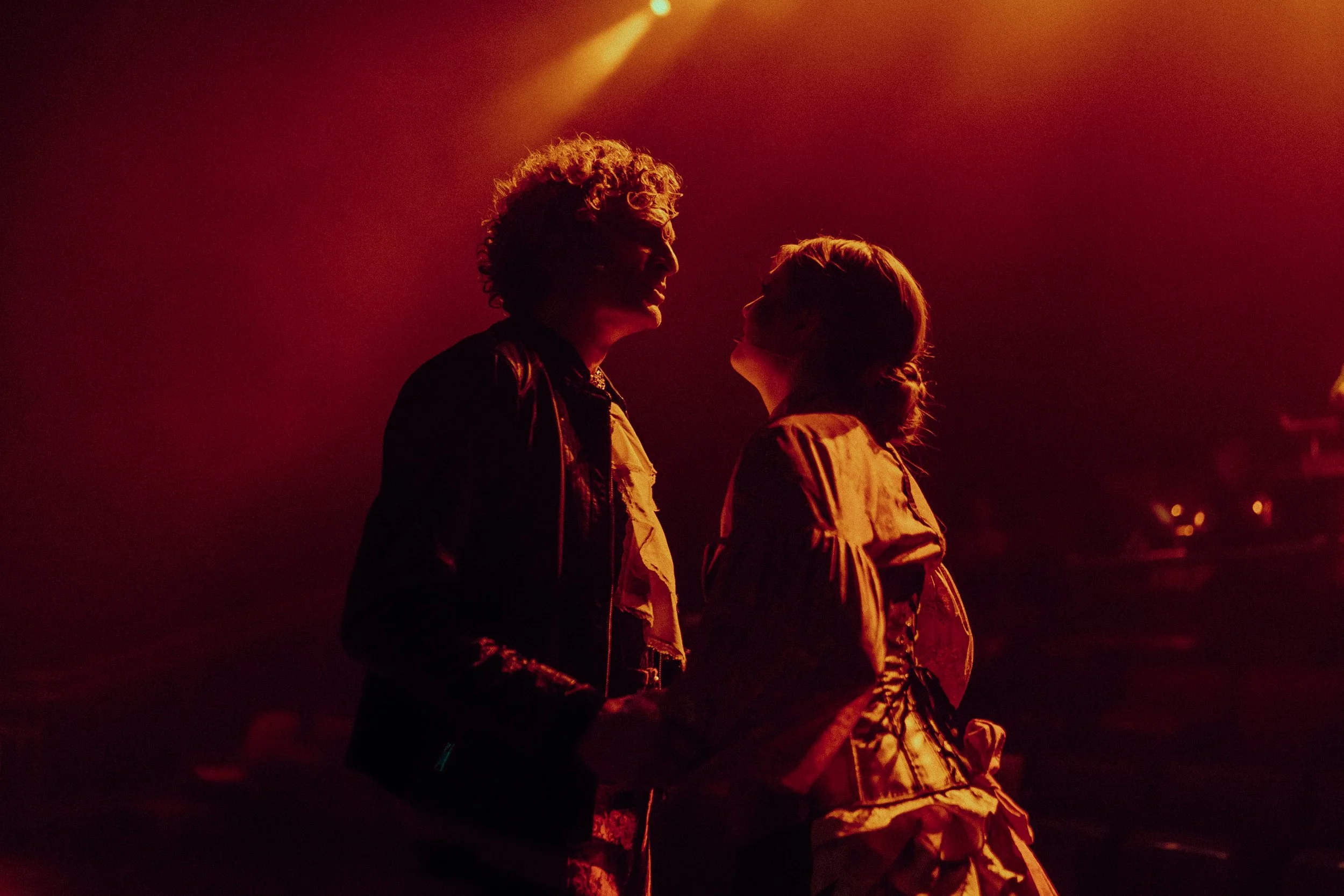 Silhouetted couple dancing under red stage lights, with dramatic backlighting.