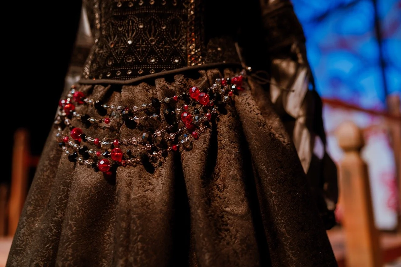 Close-up of an ornate black dress adorned with red and black beads in a pattern.