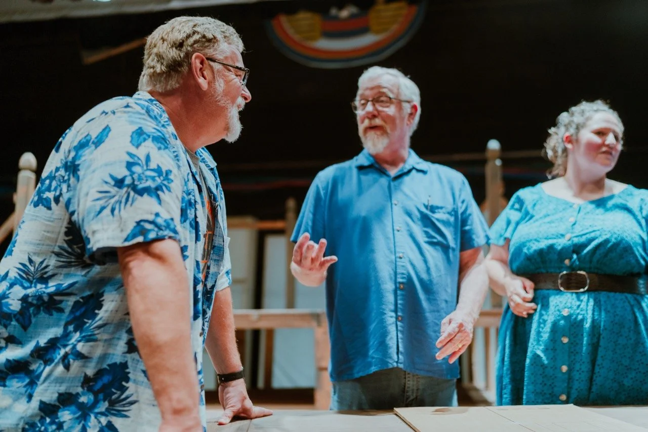 Three adults engaged in conversation, dressed in casual blue clothing, standing indoors.