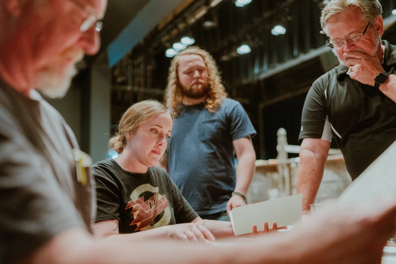 Group of people engaged in a discussion with one person reading a document, in an indoor setting.