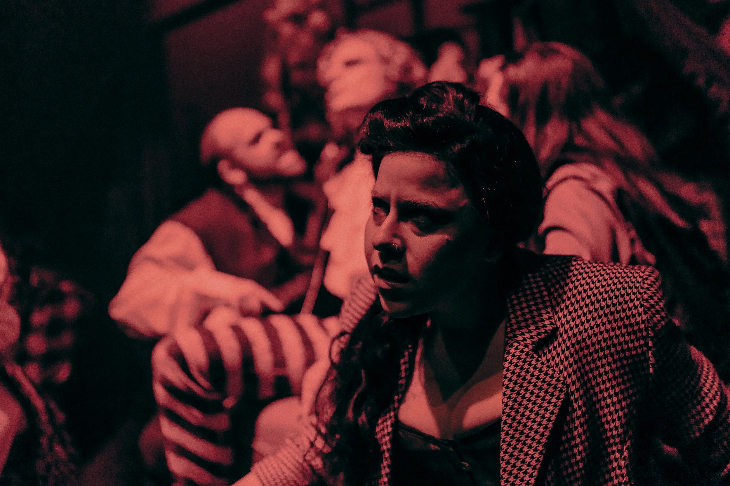 Dramatic scene with people in theatrical costumes under red lighting.
