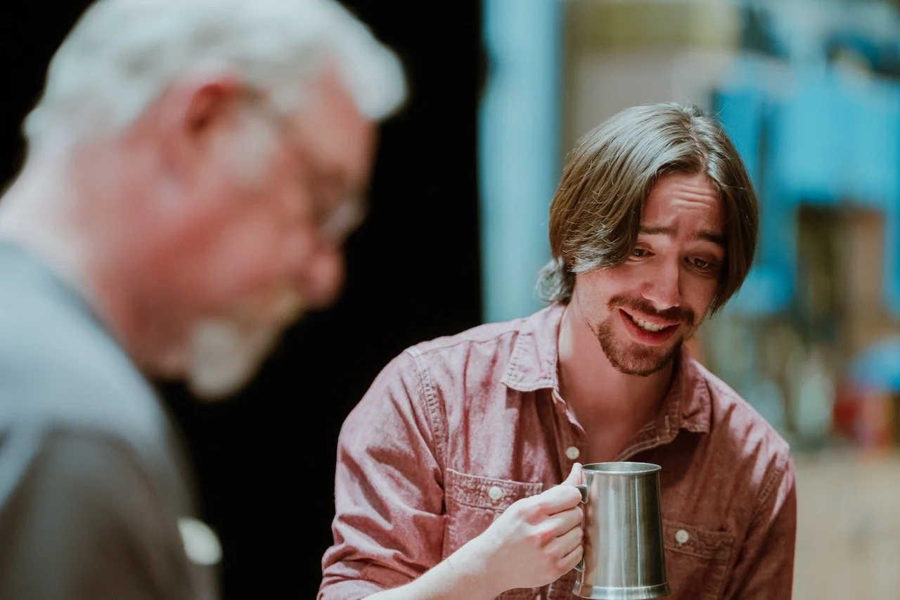 Two men interacting, one with a mug, in an indoor setting.