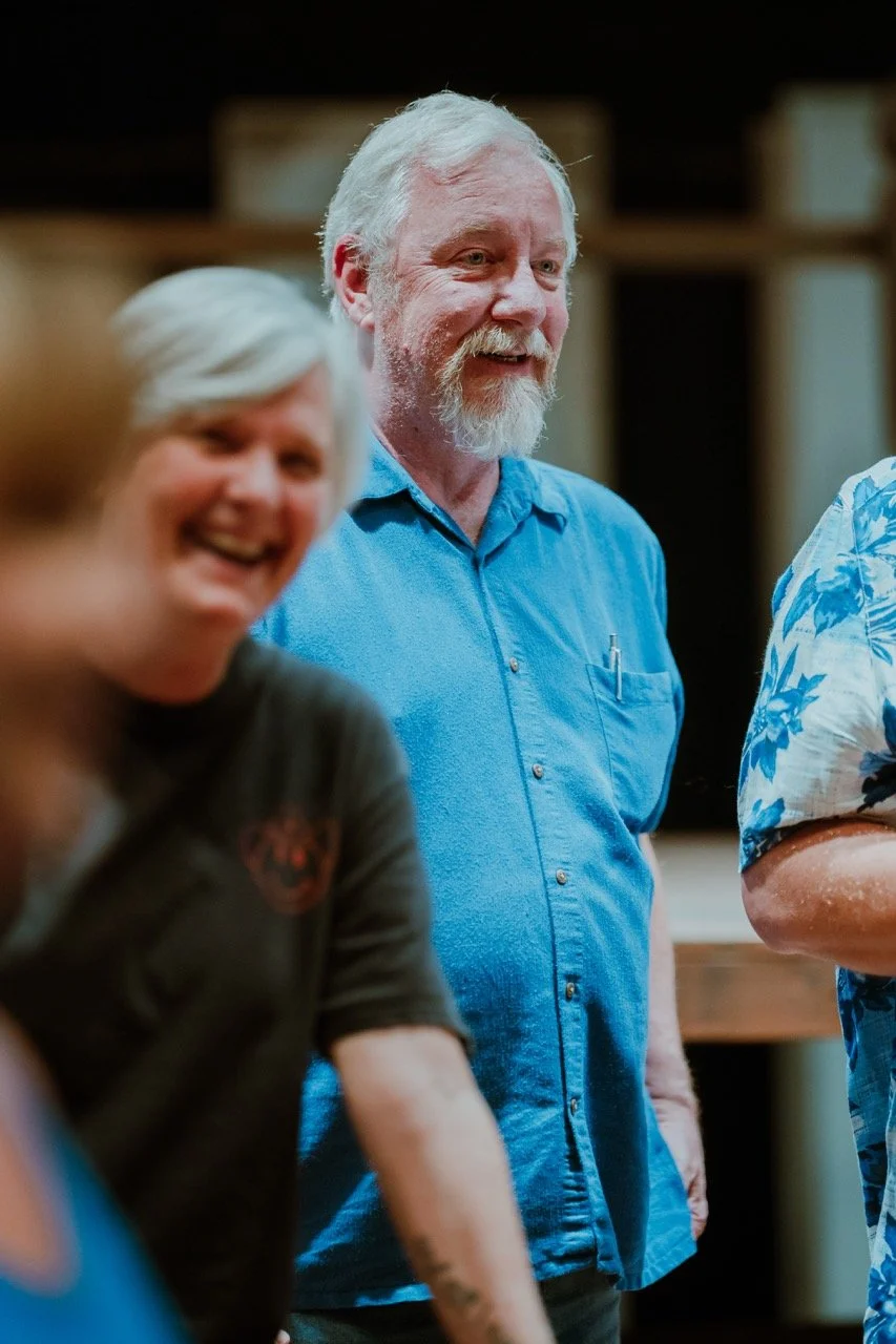 Group of smiling people standing indoors, one wearing a blue shirt.