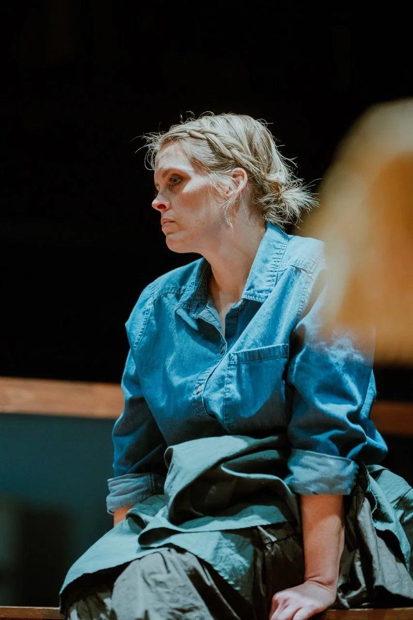 Person wearing a denim shirt sitting indoors, looking pensive.