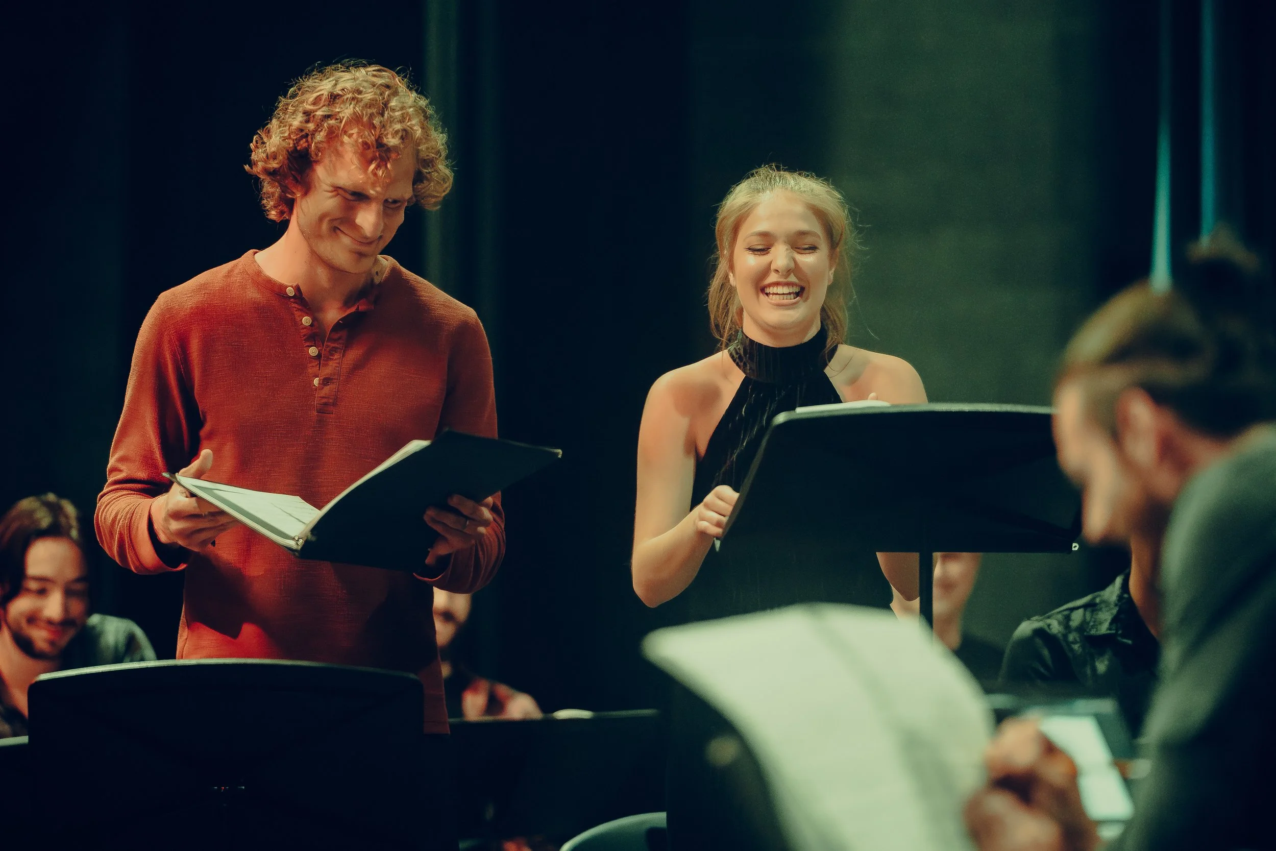 Group of actors reading scripts in a theater rehearsal.